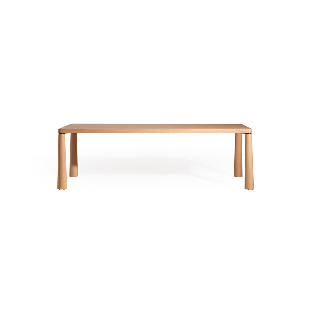 Rectangular wooden table with light-toned finish, featuring four cylindrical legs and a flat top surface. Made of wood with visible grain. Designed for dining or workspaces. Category: furniture > tables > dining tables