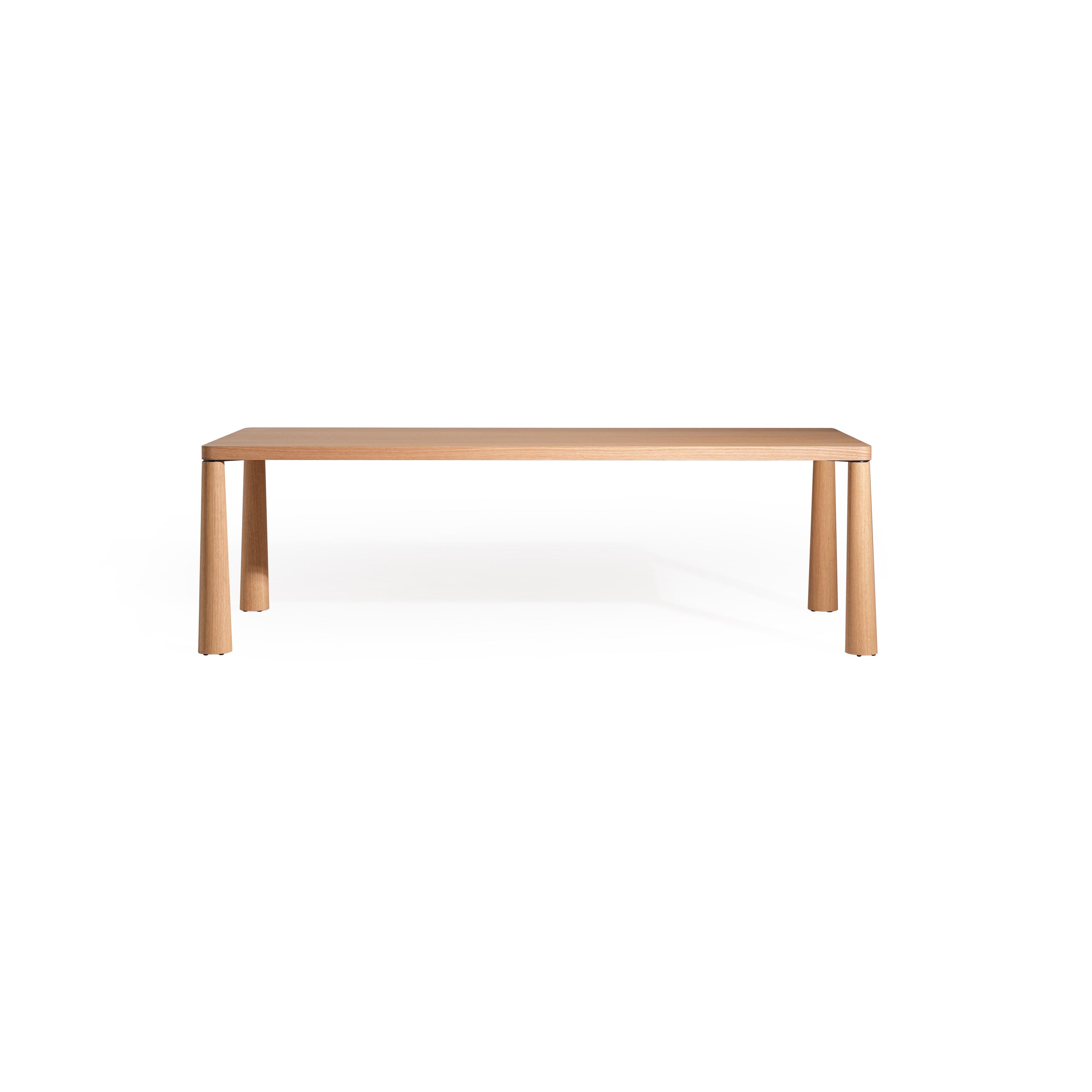 Rectangular wooden table with light-toned finish, featuring four cylindrical legs and a flat top surface. Made of wood with visible grain. Designed for dining or workspaces. Category: furniture > tables > dining tables