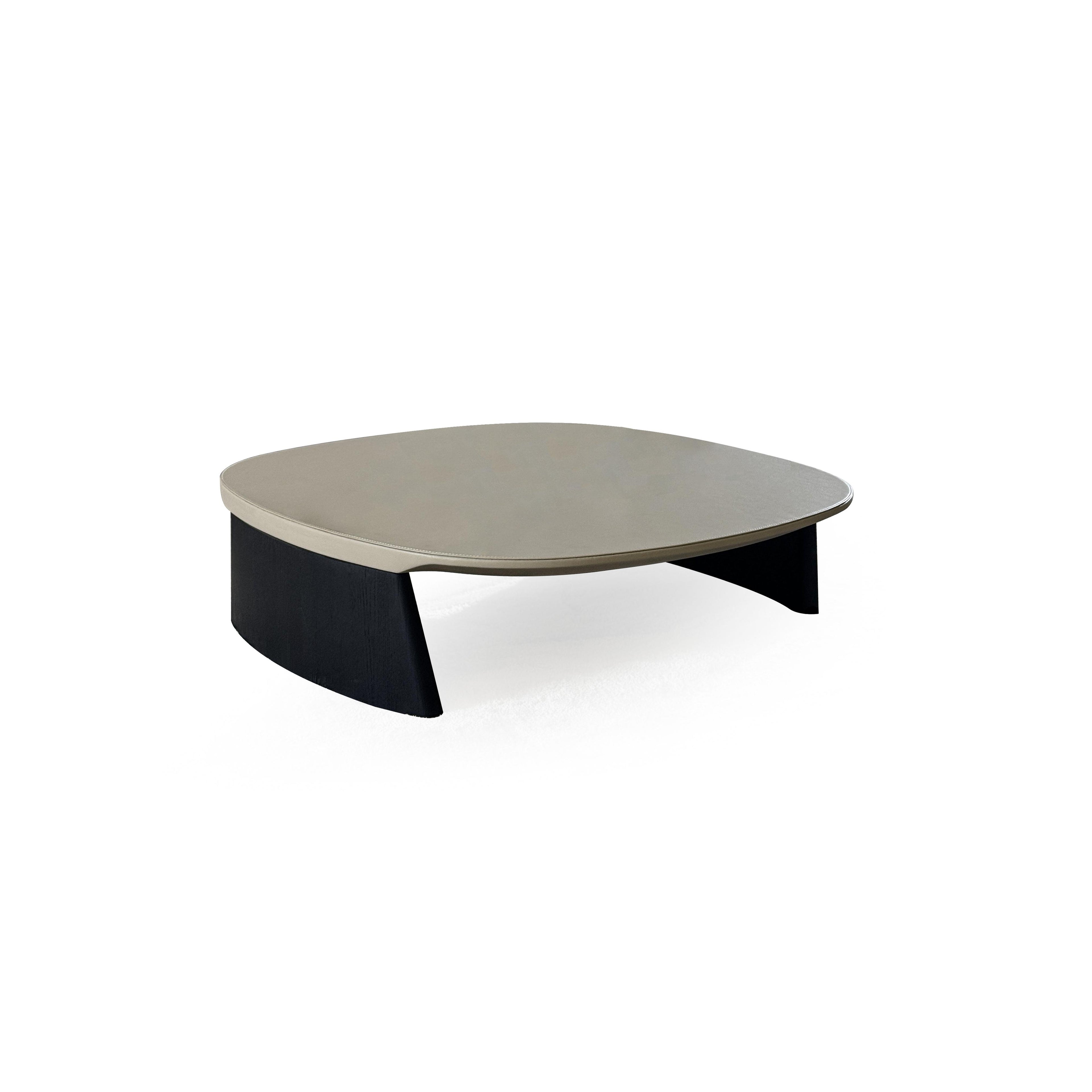 This is a low-profile stool with a rounded, flat top surface upholstered in a light beige material. It has two dark, tapered legs that curve slightly outward. The surface shows subtle stitching along the edge. Intended for seating or as a footrest, it features a minimalist design with no arms or additional hardware. Category: Furniture > Stools