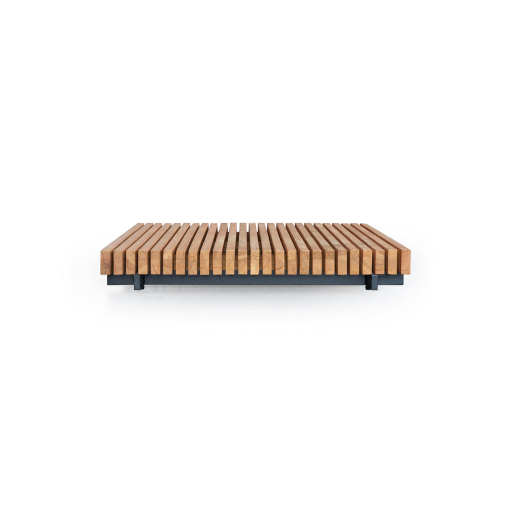 This is a low-profile bench with parallel wooden slats in a light brown finish resting on a dark gray metal frame. It has four short legs and a flat, rectangular form. The wood shows natural grain. Intended for seating in outdoor or indoor spaces. Category: Furniture > Outdoor Furniture > Benches