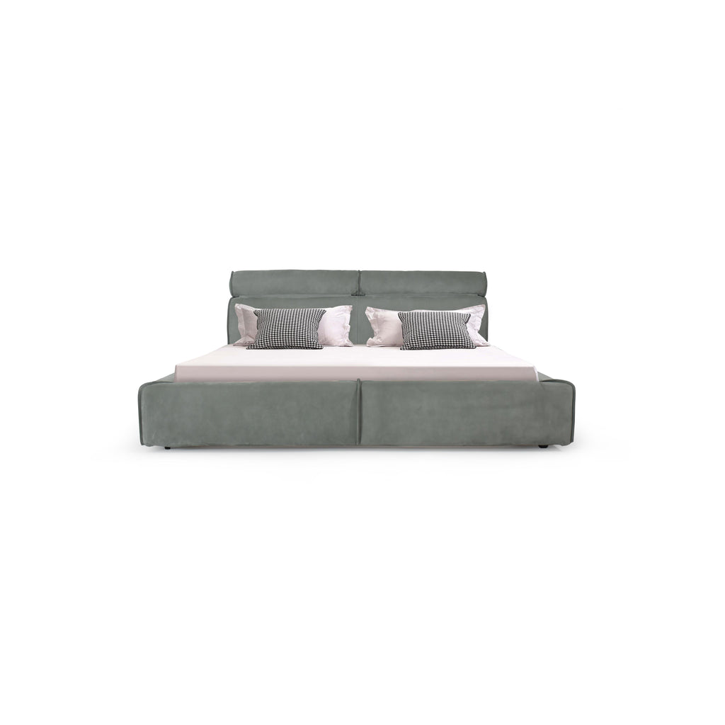 This is a upholstered bed with a low-profile frame and a padded headboard. It features a gray fabric finish, segmented cushioning along the base, and four small black feet. The bed holds a white mattress and four pillows: two solid white and two black-and-white checkered. Category: furniture > beds > upholstered beds