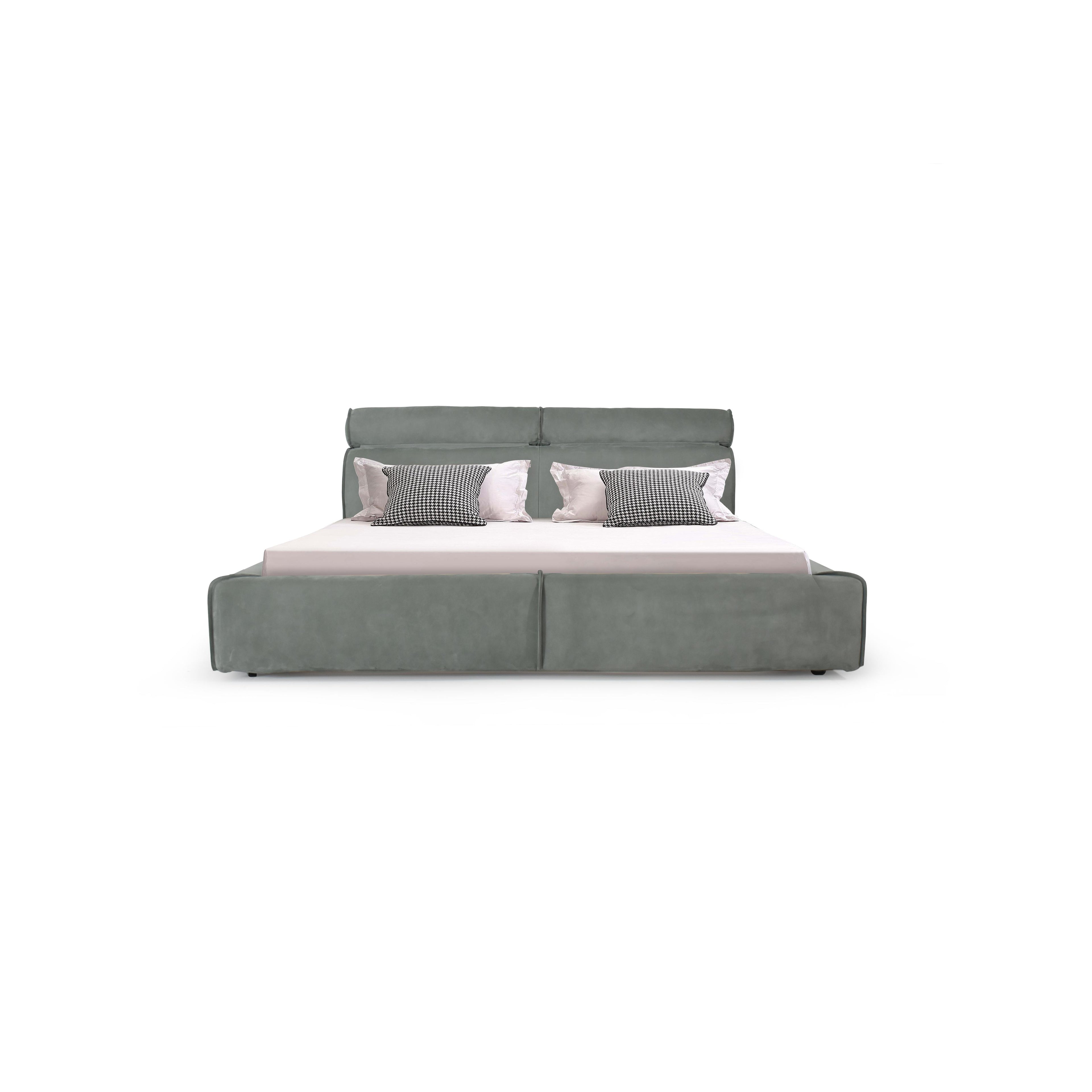 This is a upholstered bed with a low-profile frame and a padded headboard. It features a gray fabric finish, segmented cushioning along the base, and four small black feet. The bed holds a white mattress and four pillows: two solid white and two black-and-white checkered. Category: furniture > beds > upholstered beds