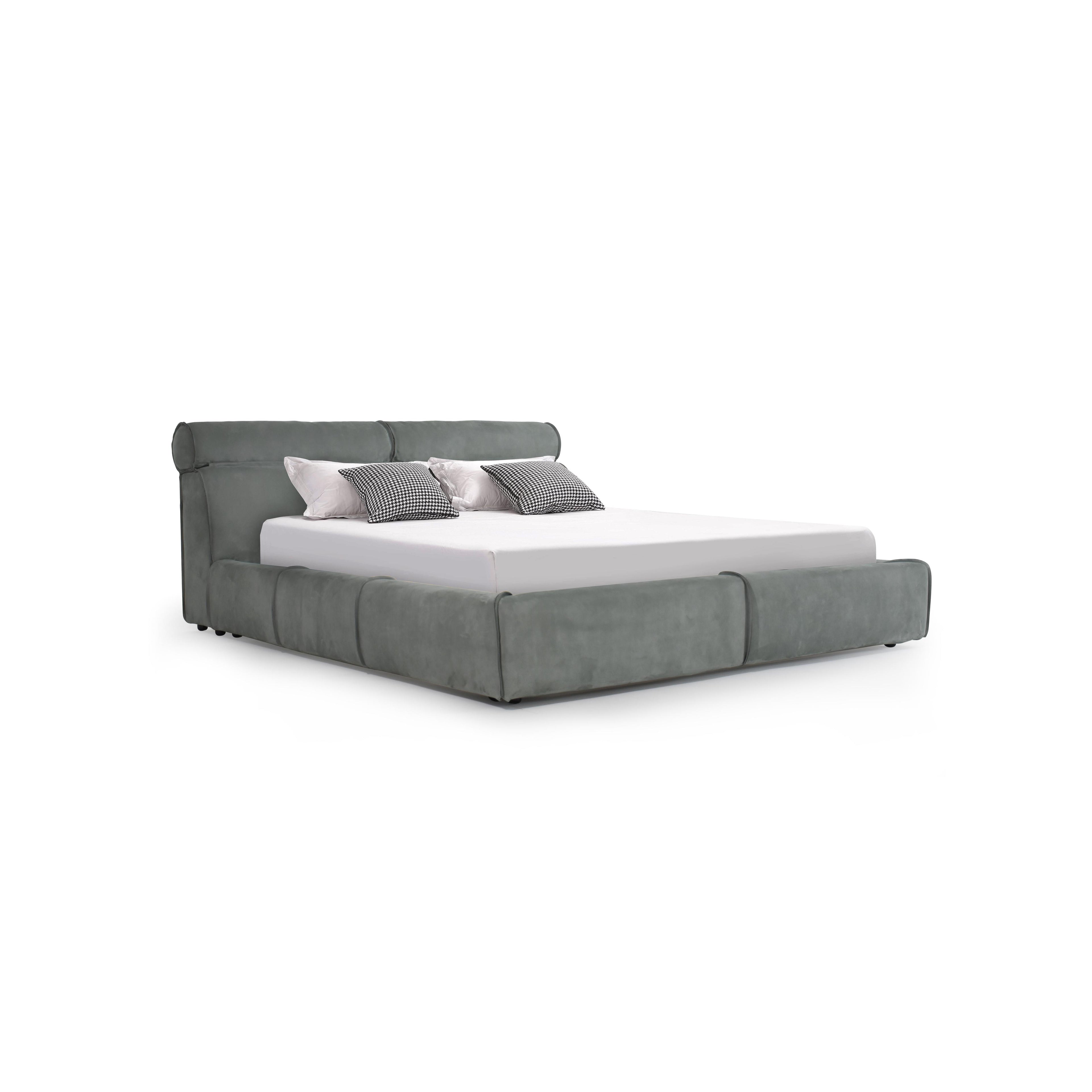 This is a upholstered bed with a low-profile frame and a padded headboard. It features a gray fabric finish, segmented cushioning along the base, and four small black feet. The bed holds a white mattress and four pillows: two solid white and two black-and-white checkered. Category: furniture > beds > upholstered beds
