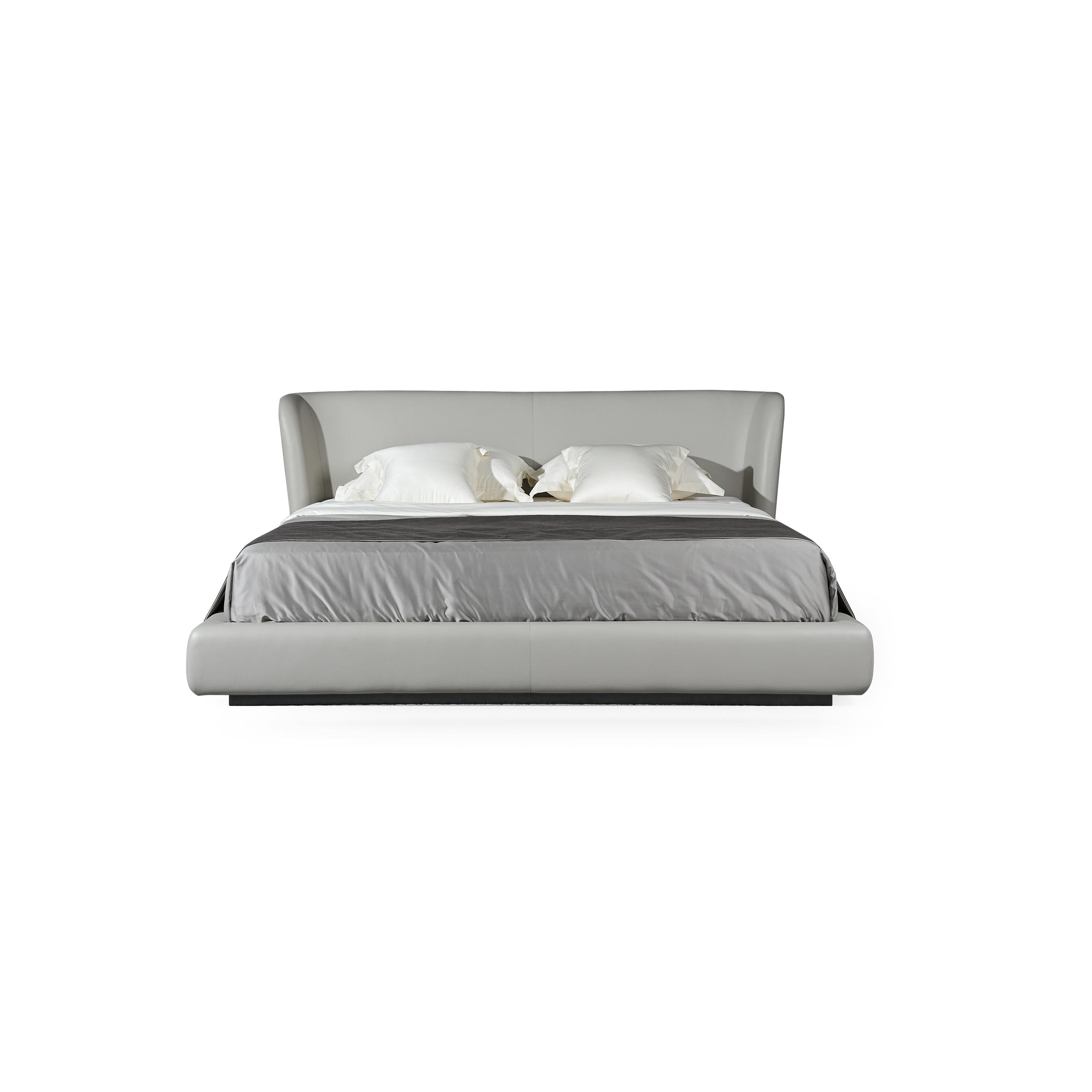 A low-profile bed with a continuous upholstered headboard and base, featuring a light gray fabric surface, two white pillows, and a dark gray throw blanket; supported by a dark base; designed for sleeping; Category: furniture > beds > platform beds