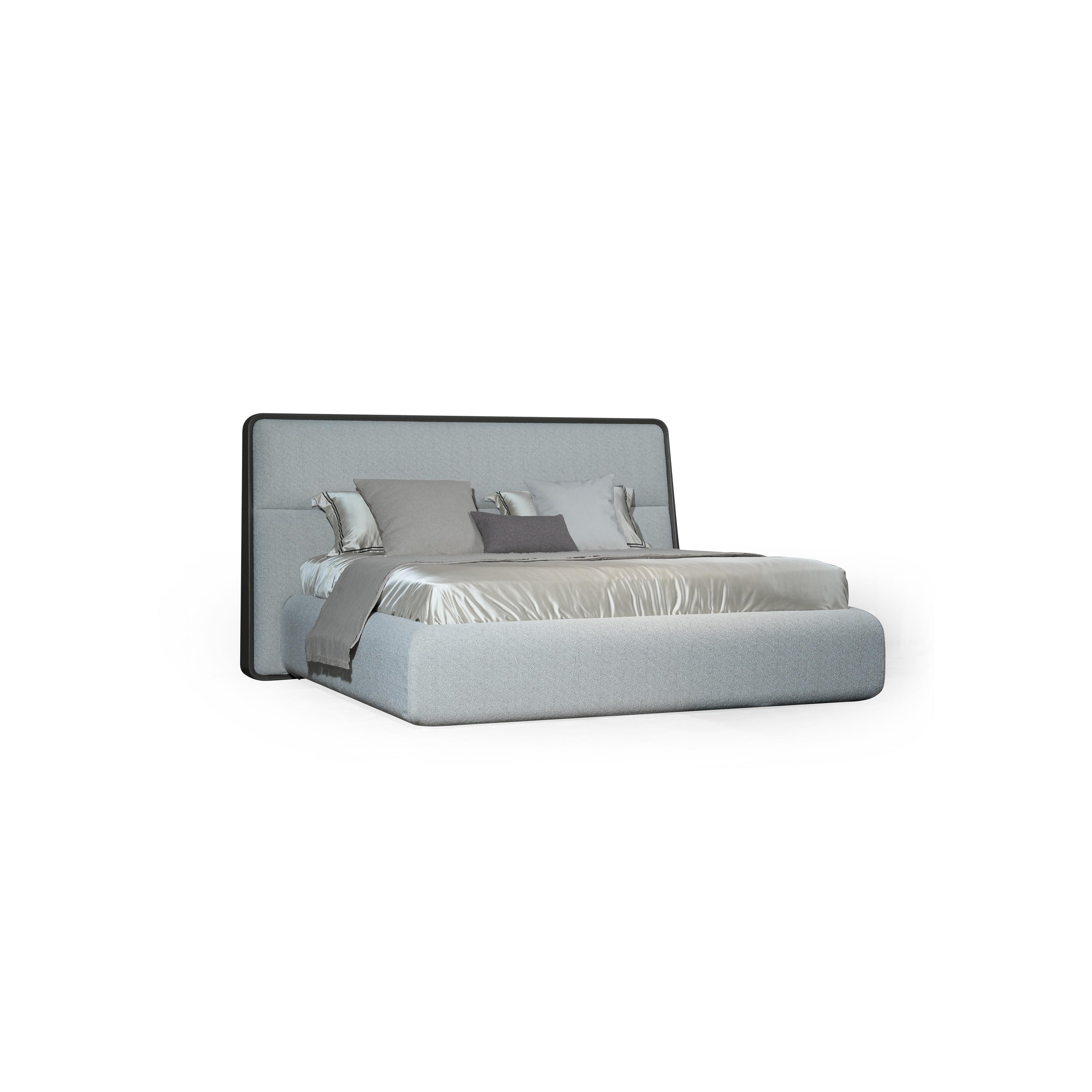 A upholstered bed with a rectangular headboard and matching base, featuring light gray fabric upholstery, multiple pillows in varying shades of gray and white, and a satin-like bedspread. Category: furniture > beds > upholstered beds