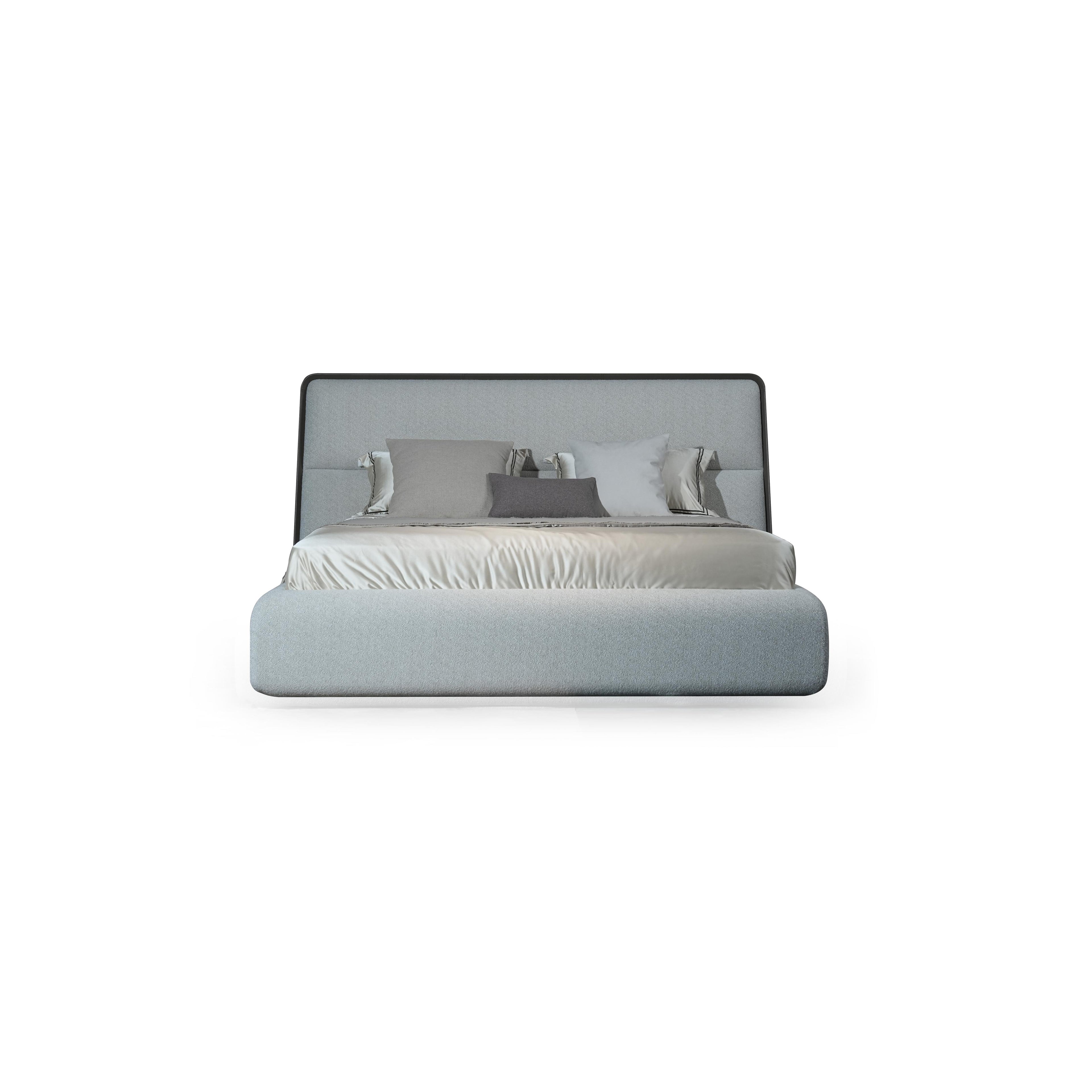 A upholstered bed with a rectangular headboard and matching base, featuring light gray fabric upholstery, multiple pillows in varying shades of gray and white, and a satin-like bedspread. Category: furniture > beds > upholstered beds