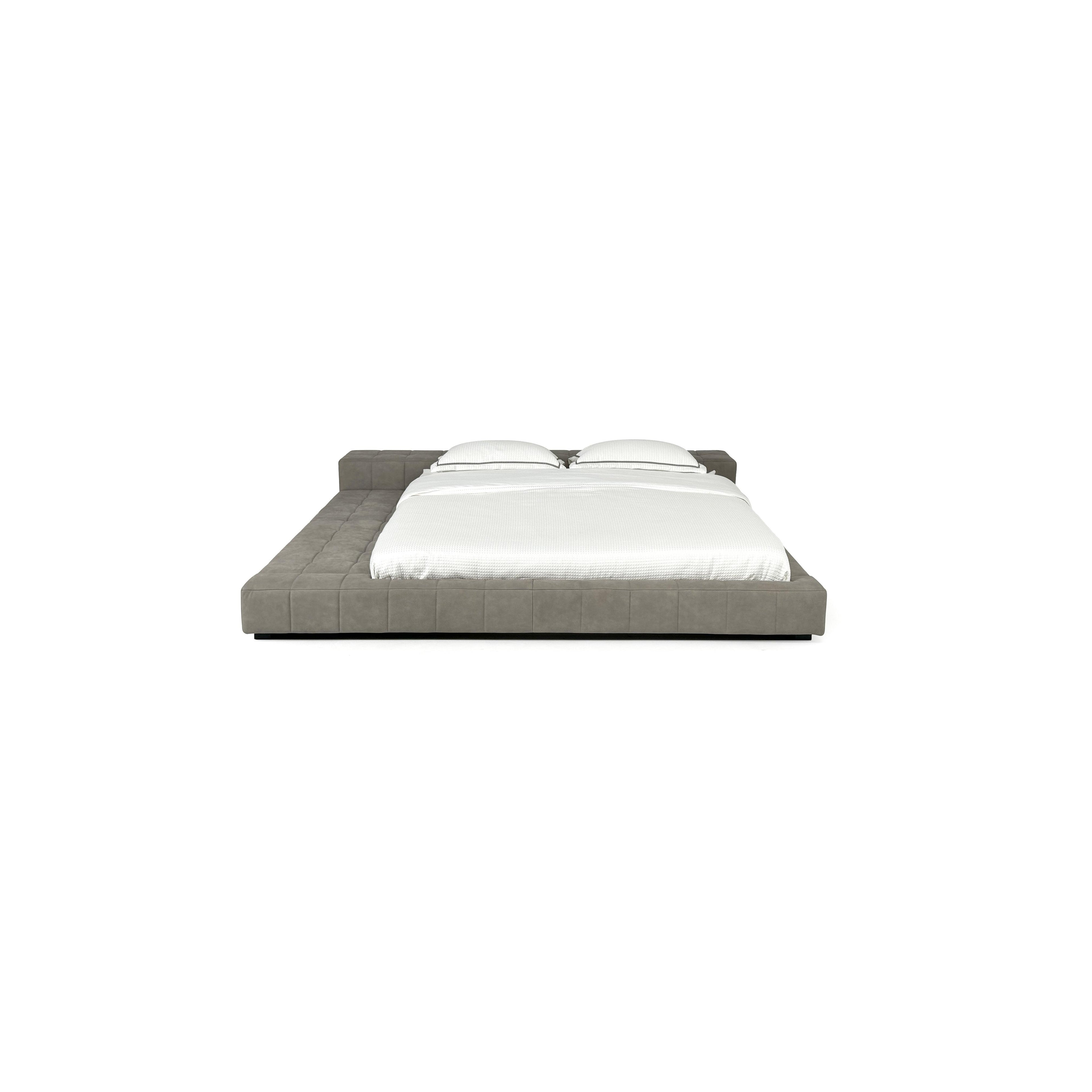 Low-profile platform bed with tufted gray upholstered frame, two matching pillows, and white bedding; features short black legs and continuous cushioned base; designed for sleeping; Category: Furniture > Beds > Platform Beds