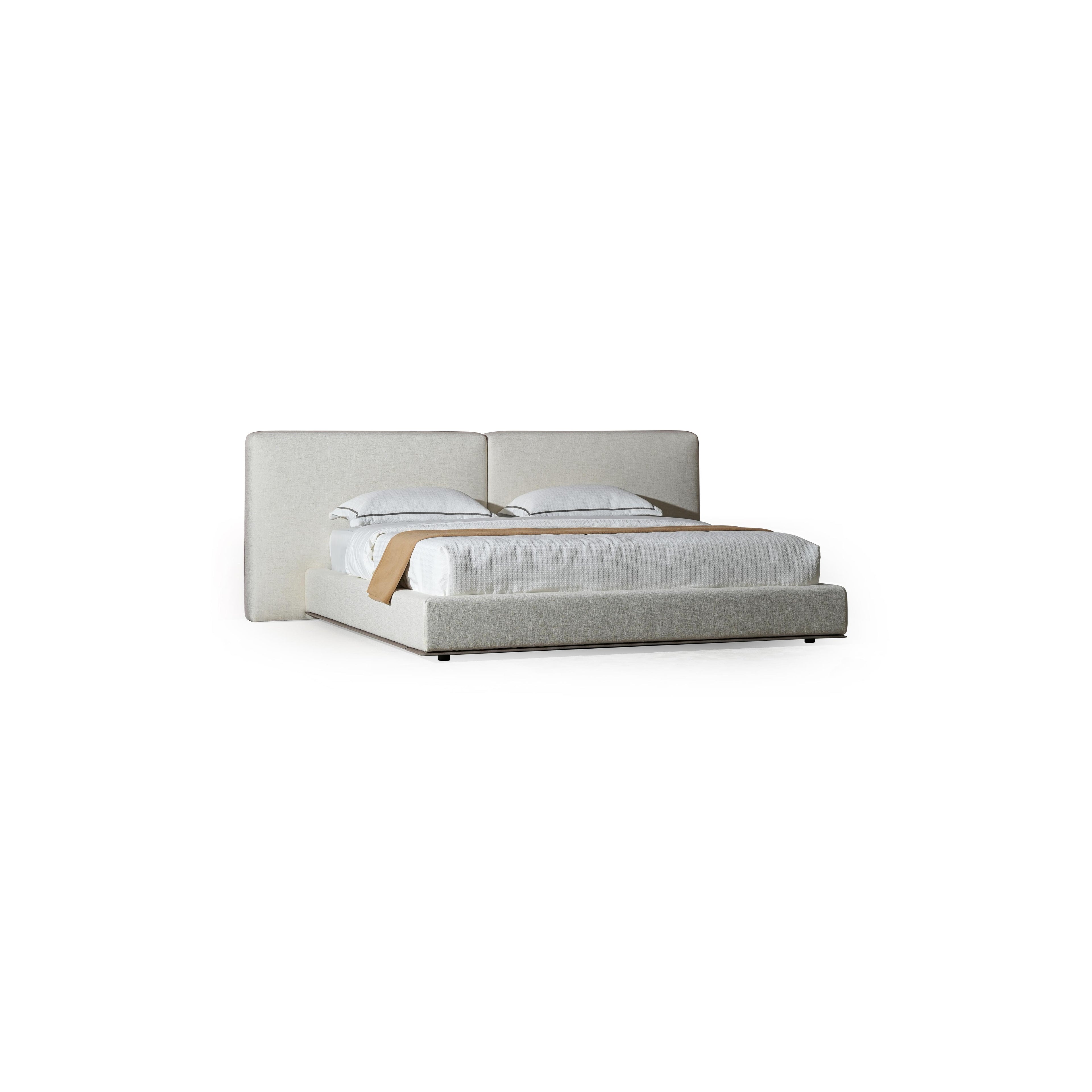 A upholstered bed with a low-profile frame and a continuous headboard, featuring two pillows and a textured white mattress with a tan throw. The base has dark legs and a fabric-covered structure. Category: furniture > beds > upholstered beds