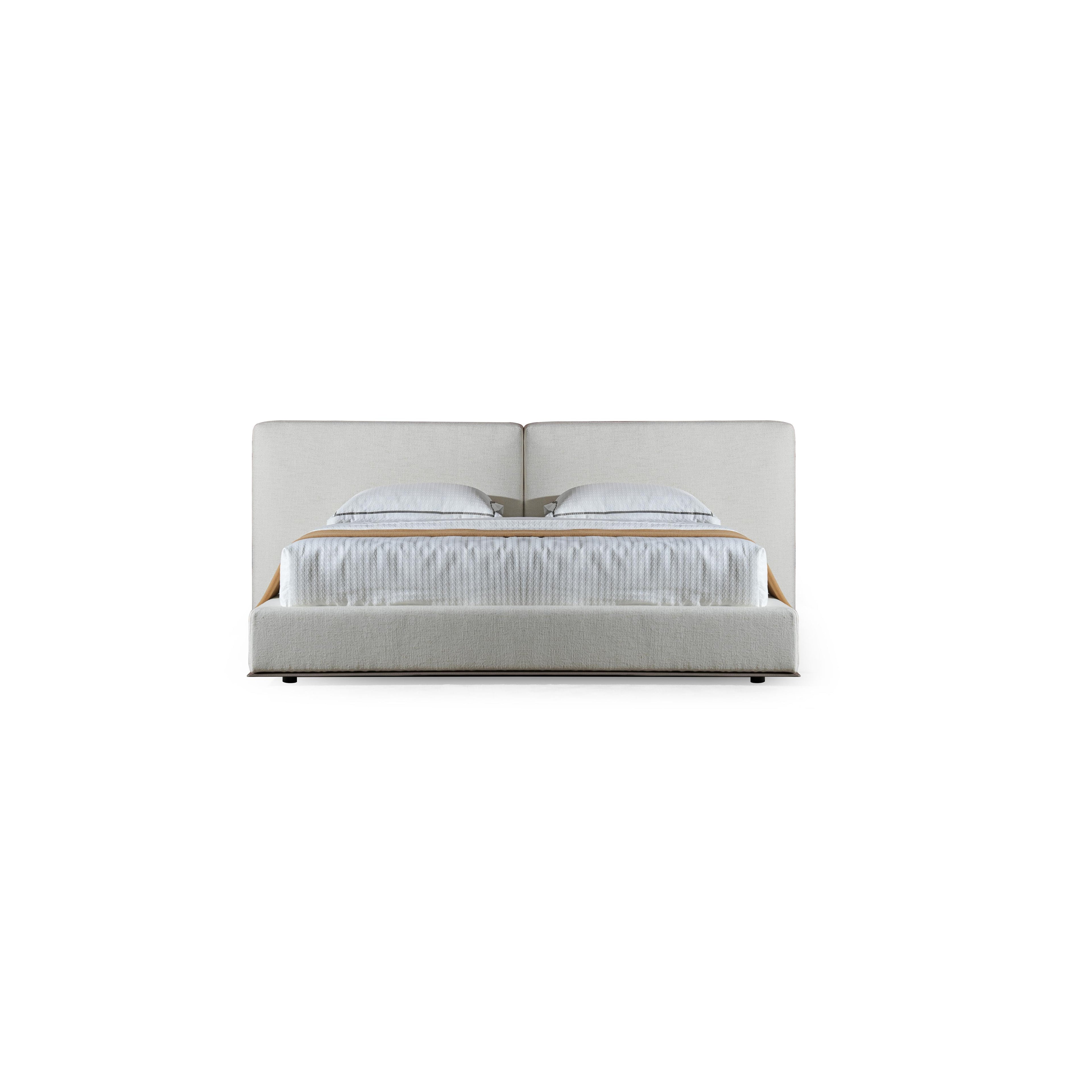A upholstered bed with a low-profile frame and a continuous headboard, featuring two pillows and a textured white mattress with a tan throw. The base has dark legs and a fabric-covered structure. Category: furniture > beds > upholstered beds