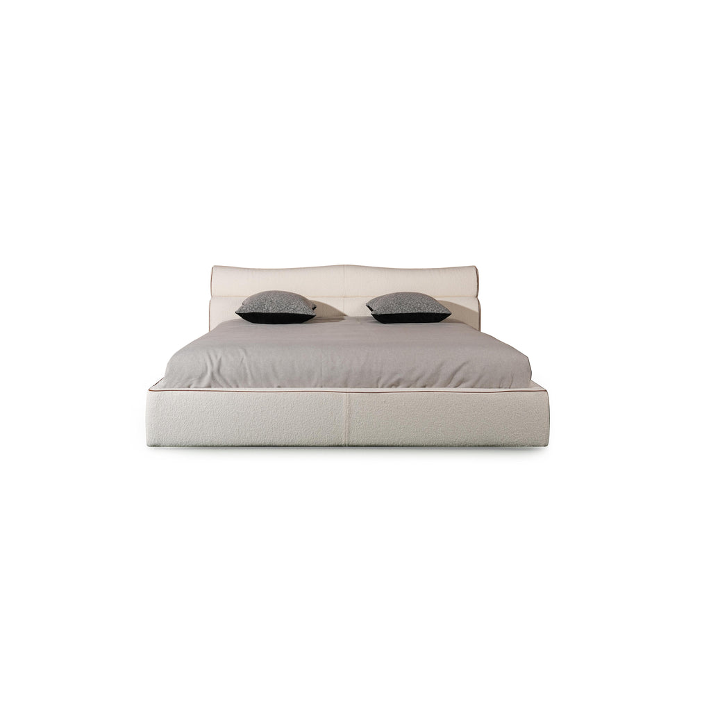 Upholstered bed with a low-profile rectangular frame, featuring a padded headboard and base, covered in a textured fabric with subtle stitching. Two dark gray pillows rest on the mattress. Category: furniture > beds > upholstered beds