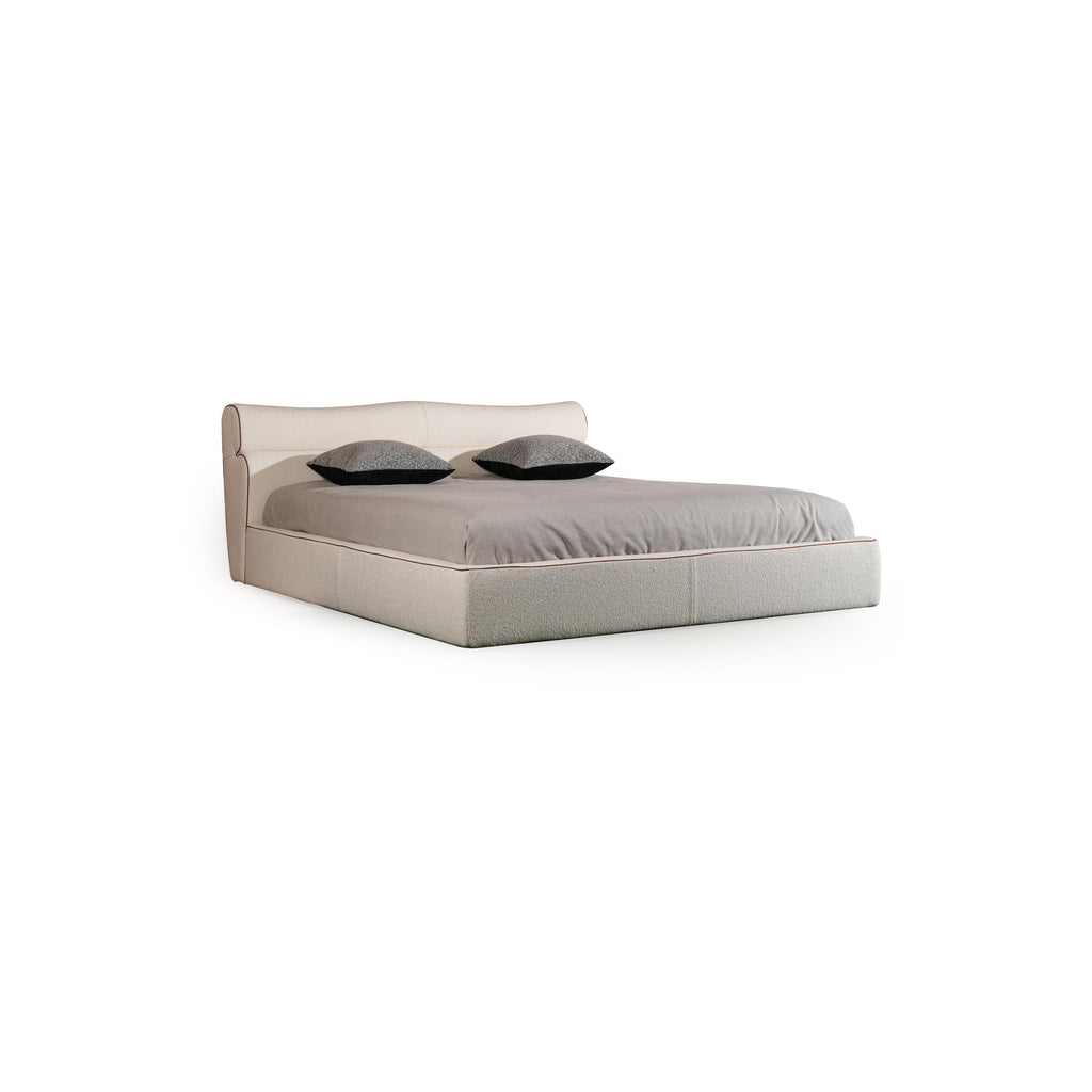 Upholstered bed with a low-profile rectangular frame, featuring a padded headboard and base, covered in a textured fabric with subtle stitching. Two dark gray pillows rest on the mattress. Category: furniture > beds > upholstered beds