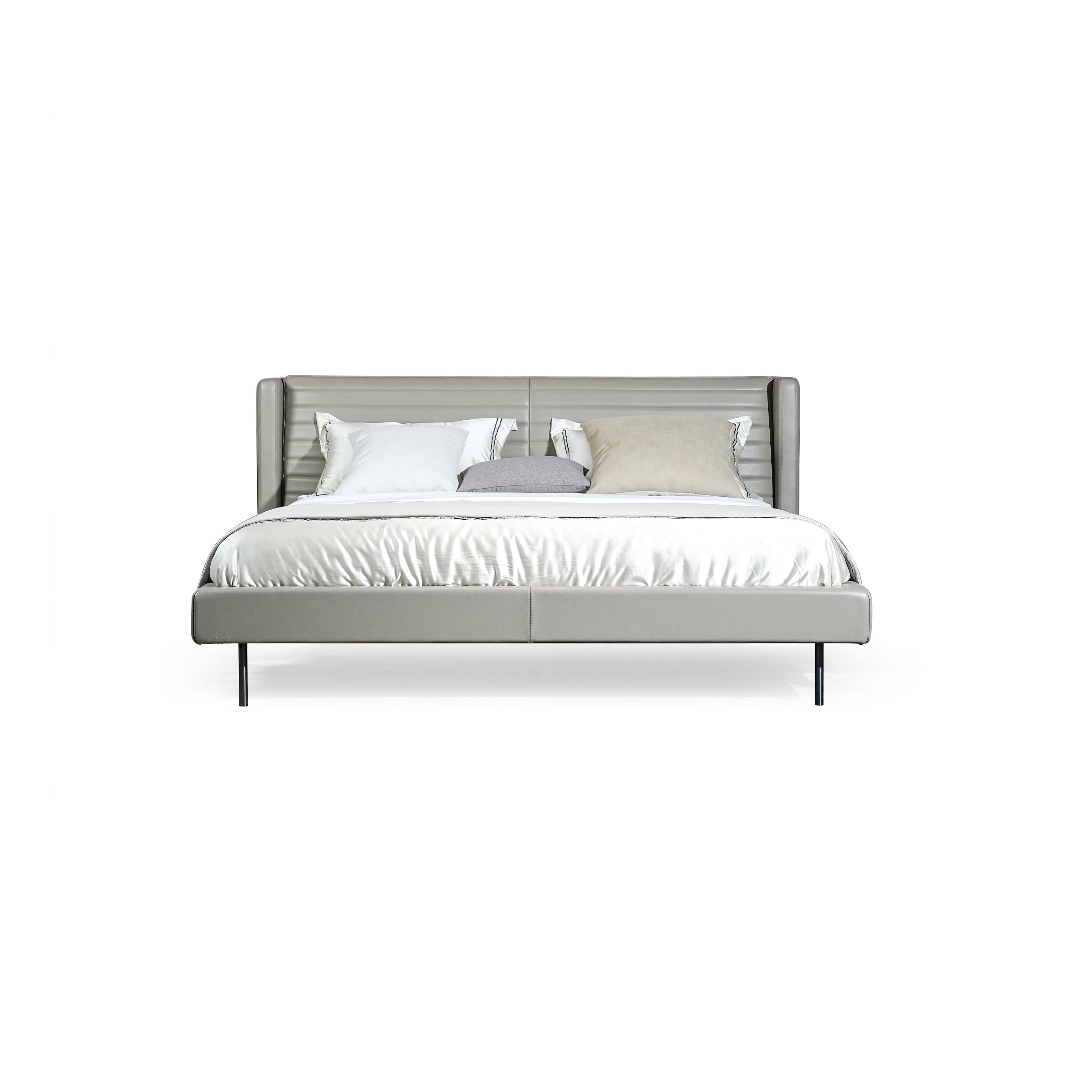 A modern bed with a gray upholstered headboard and base, supported by four thin black legs. It features a tufted backrest, layered pillows, and a satin-textured duvet. Designed for sleeping, it has a clean, minimalist silhouette with visible stitching along seams. Category: Furniture > Beds > Modern Beds