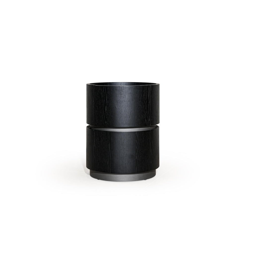 This is a cylindrical side table with two stacked sections, finished in black wood grain and metallic bands. It has a flat top surface and a circular base. Intended for holding items, it features a minimalist design with visible wood texture and metal accents. Category: Furniture > Tables > Side Tables