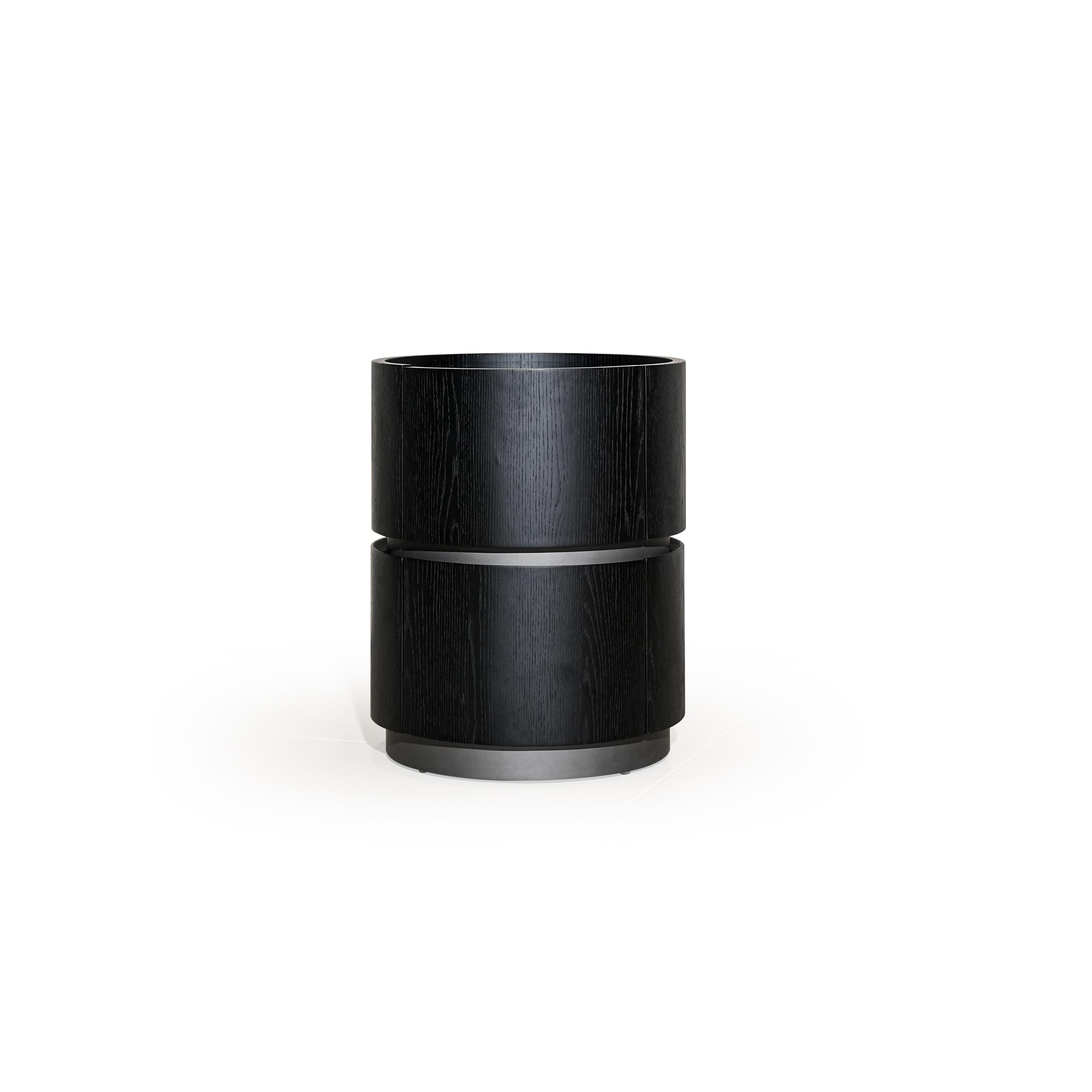 This is a cylindrical side table with two stacked sections, finished in black wood grain and metallic bands. It has a flat top surface and a circular base. Intended for holding items, it features a minimalist design with visible wood texture and metal accents. Category: Furniture > Tables > Side Tables