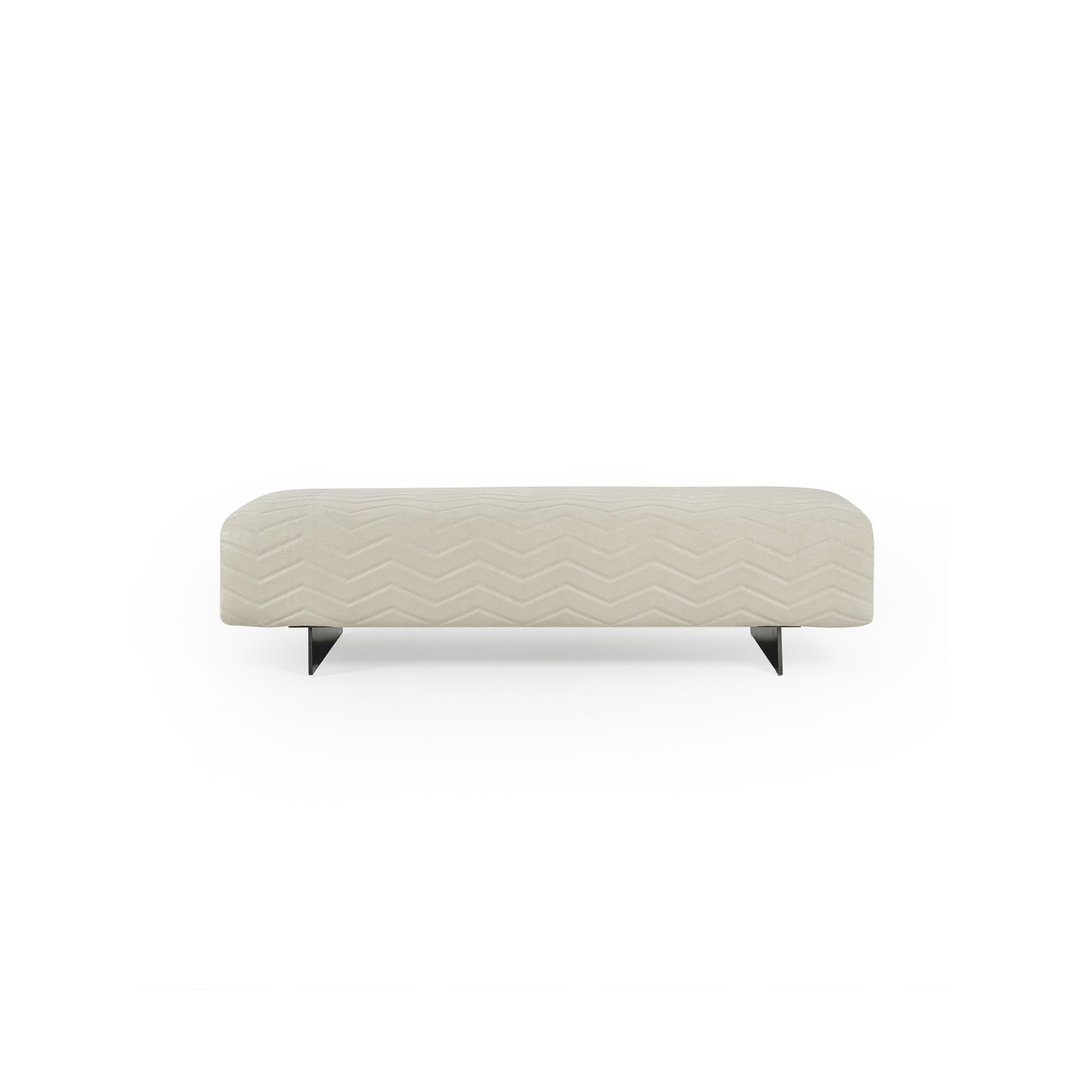 This is a long, rectangular upholstered bench with a light beige fabric surface featuring a stitched zigzag pattern. It rests on two black, angular legs. Designed for seating, it offers a modern aesthetic with clean lines and textured fabric. Category: Furniture > Seating > Bench