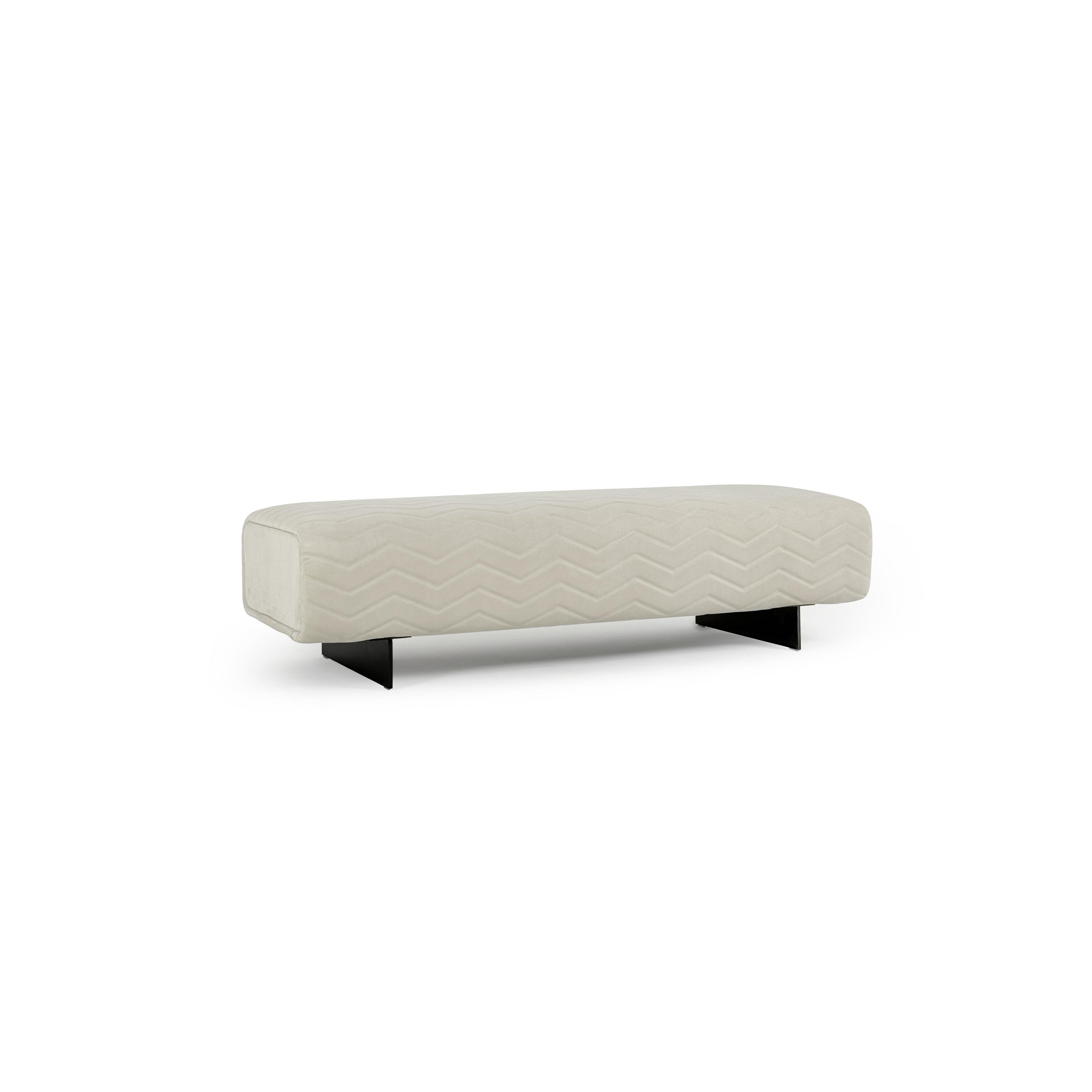 This is a long, rectangular upholstered bench with a light beige fabric surface featuring a stitched zigzag pattern. It rests on two black, angular legs. Designed for seating, it offers a modern aesthetic with clean lines and textured fabric. Category: Furniture > Seating > Bench