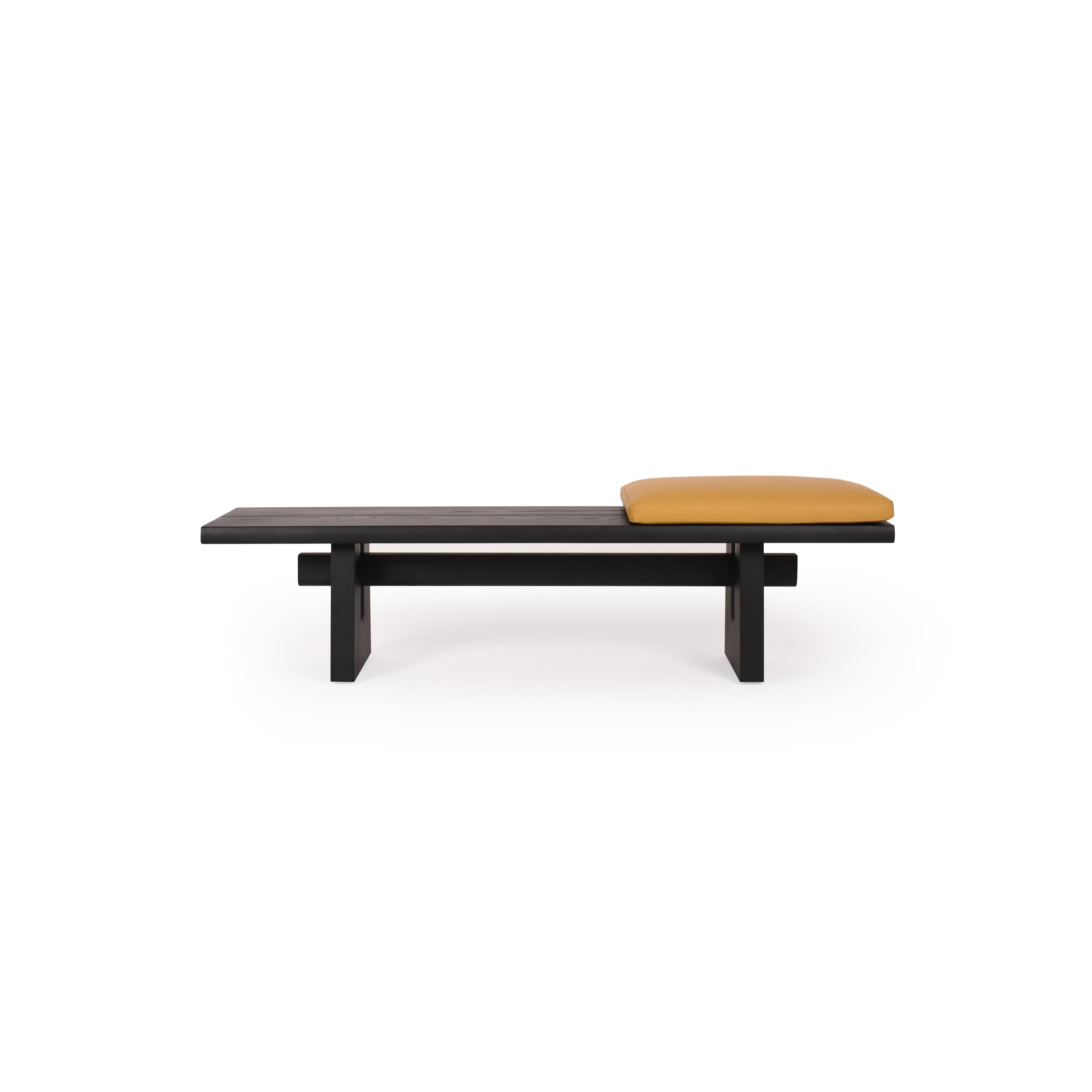 Black wooden bench with a single mustard-colored cushion resting on its seat. Features thick, blocky legs and a horizontal support beam beneath the seat. No arms, backrest, or drawers. Intended for seating. Category: furniture/benches