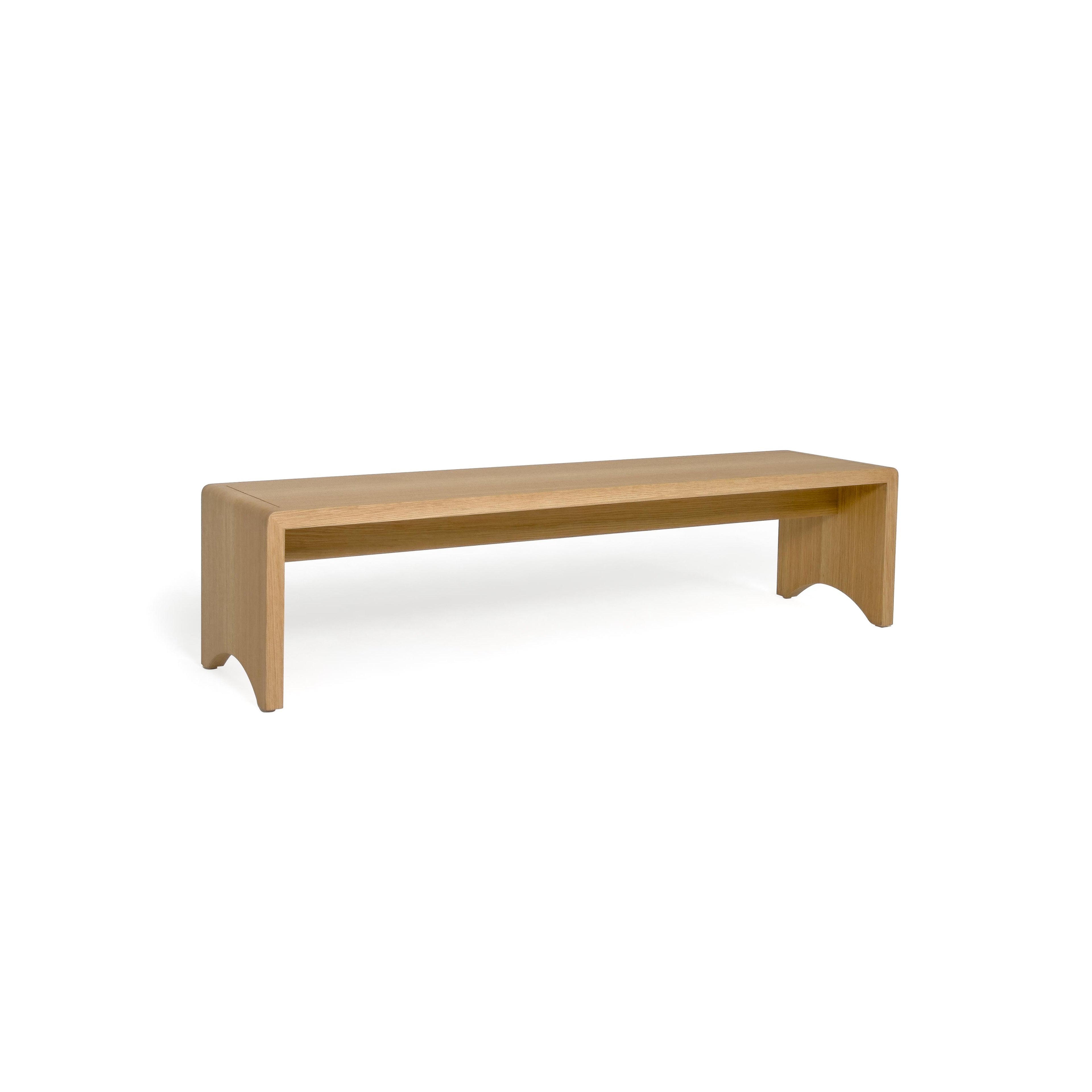 A wooden bench with a tufted beige cushion sits on four angled legs. The frame is made of light-toned wood with visible grain. The cushion has stitched seams and is held by two leather-like straps. Intended for seating, it features a simple, elongated rectangular form. Category: Furniture > Benches > Seating