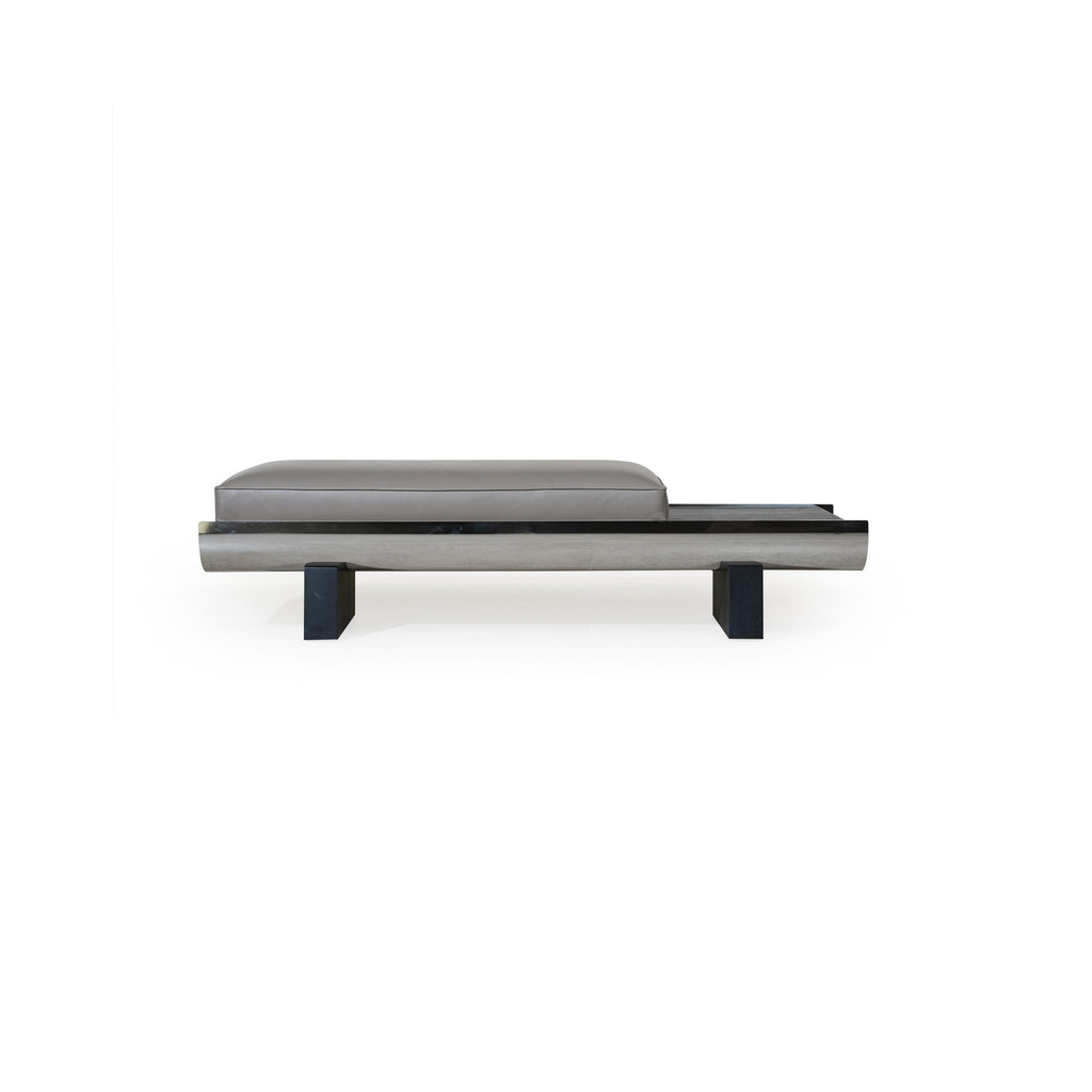 Modern bench with rectangular cushioned seat in gray upholstery, supported by a sleek metallic frame and dark wooden legs; features a curved front edge and a horizontal metallic strip along the base; designed for seating or as a low-profile accent piece. Category: Furniture > Benches