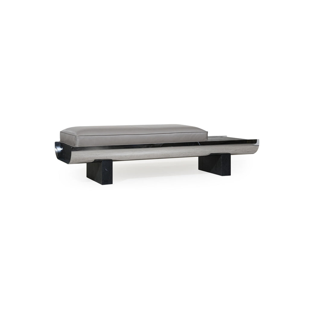 Modern bench with rectangular cushioned seat in gray upholstery, supported by a sleek metallic frame and dark wooden legs; features a curved front edge and a horizontal metallic strip along the base; designed for seating or as a low-profile accent piece. Category: Furniture > Benches