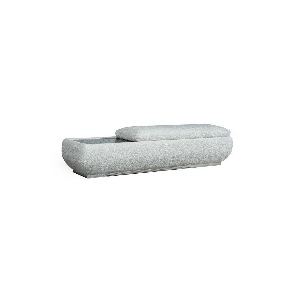 This is a low-profile bench with a soft, textured fabric upholstery in light gray. It features a rectangular base with a slightly raised cushioned section on the right. The left side reveals an open storage compartment with a grid pattern. Designed for seating and storage, it has no visible legs or frame. Category: Furniture > Seating > Bench