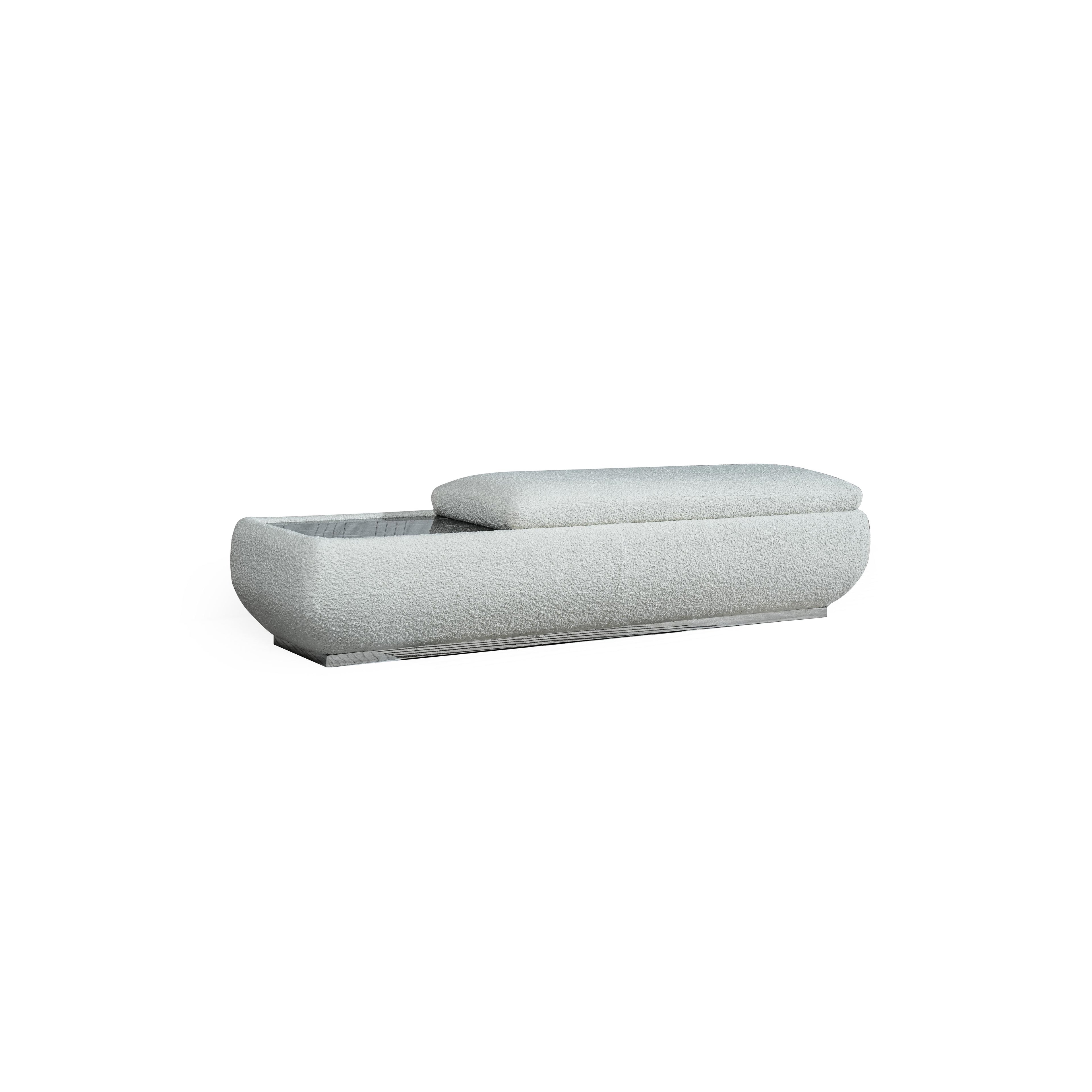 This is a low-profile bench with a soft, textured fabric upholstery in light gray. It features a rectangular base with a slightly raised cushioned section on the right. The left side reveals an open storage compartment with a grid pattern. Designed for seating and storage, it has no visible legs or frame. Category: Furniture > Seating > Bench