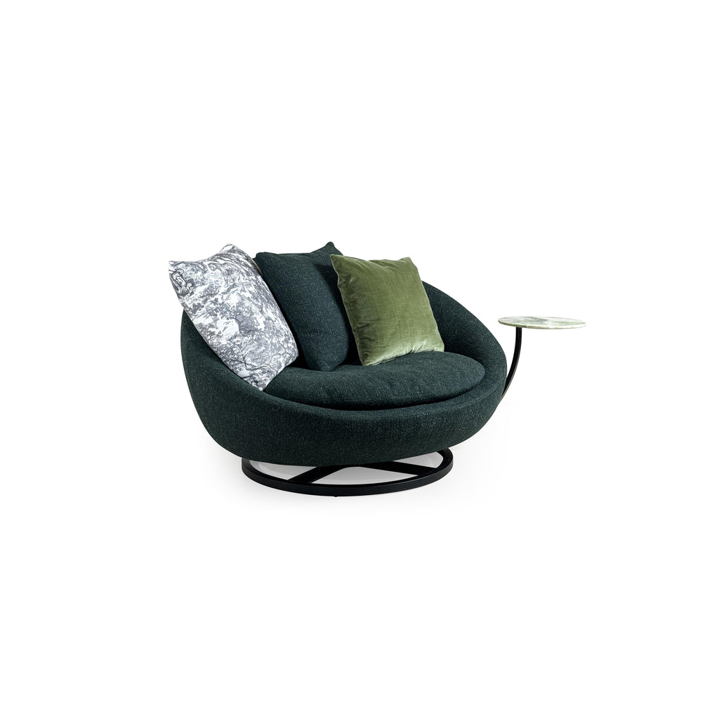 Circular swivel lounge chair with dark green textured fabric upholstery, black metal base with X-shaped support, and integrated side table with light green marble top; features three cushions including one with gray and white pattern and one solid olive green; designed for seated relaxation and casual use. Category: Furniture > Sofas & Sectionals > Lounge Chairs