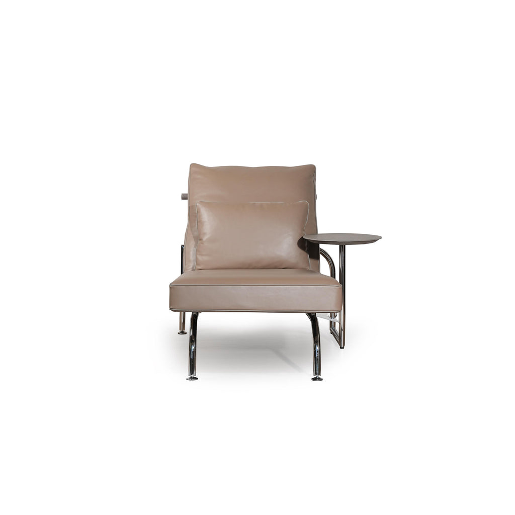 Modern armchair with tan upholstered seat and backrest, featuring a small matching cushion, chrome-finished legs, and a side table attached to the right armrest. The chair has a sleek, minimalist form with visible stitching along seams. Intended for seated relaxation or reading. Category: Furniture > Chairs > Armchairs