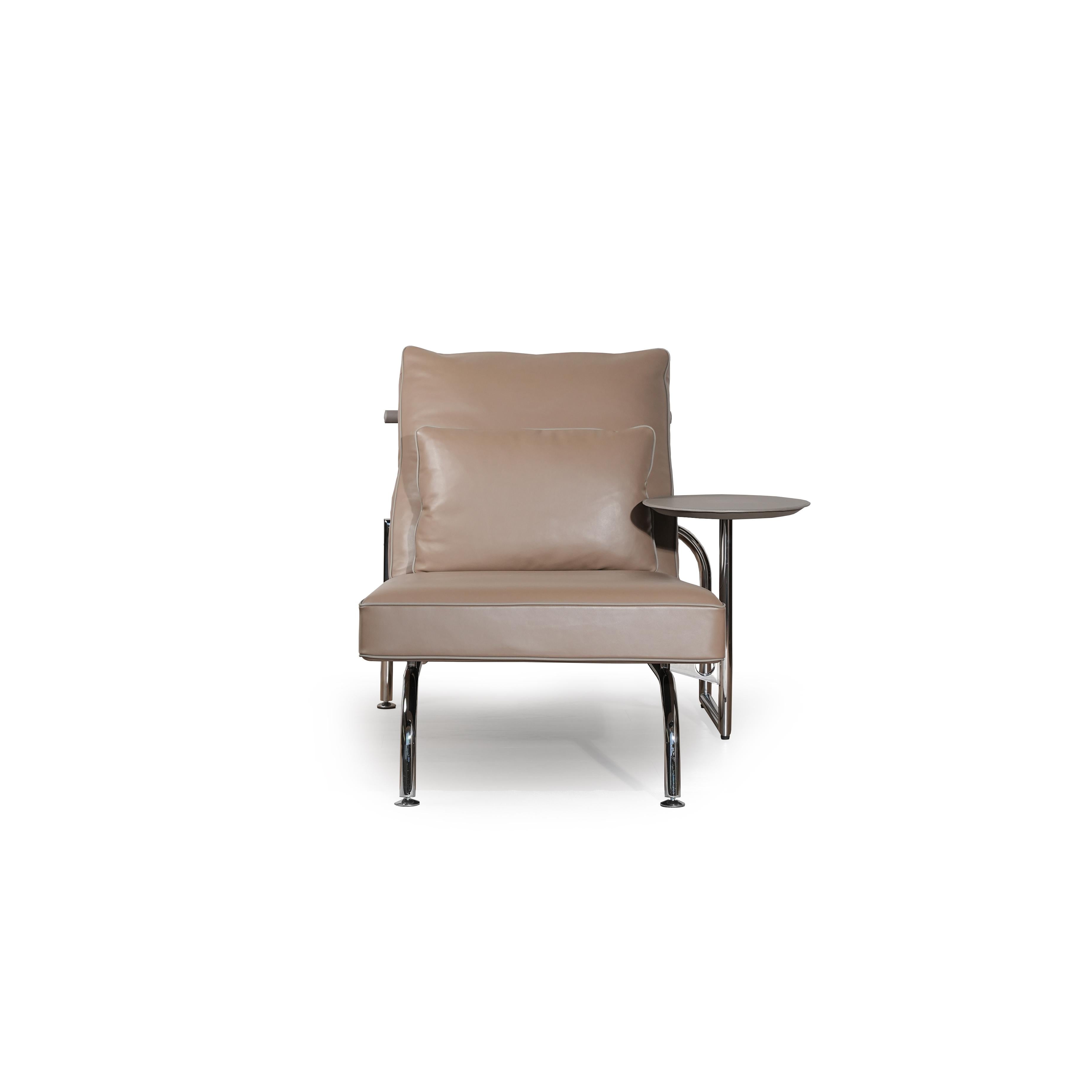 Modern armchair with tan upholstered seat and backrest, featuring a small matching cushion, chrome-finished legs, and a side table attached to the right armrest. The chair has a sleek, minimalist form with visible stitching along seams. Intended for seated relaxation or reading. Category: Furniture > Chairs > Armchairs