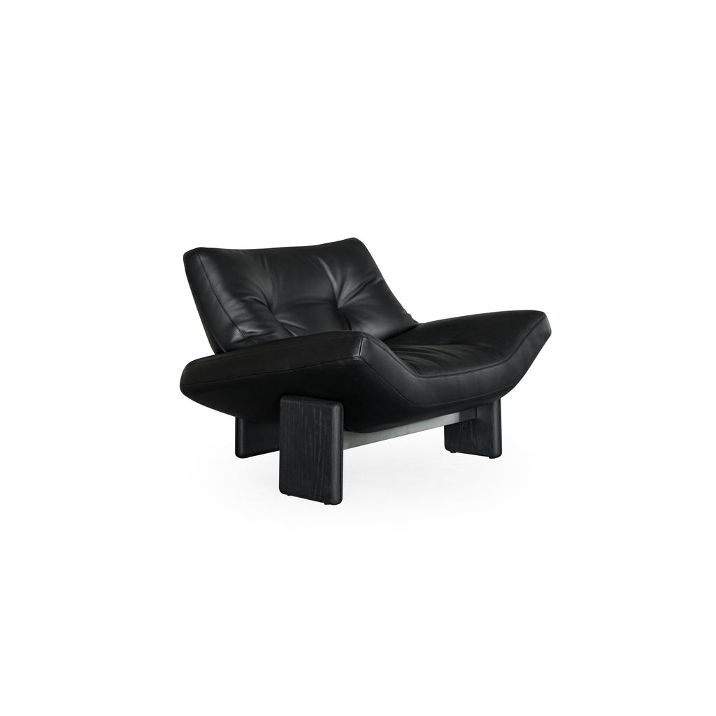 Black leather-like upholstered lounge chair with tufted backrest and curved seat, supported by two dark wooden block legs and a metal frame; designed for reclining or lounging; Category: Furniture > Chairs > Lounge Chairs