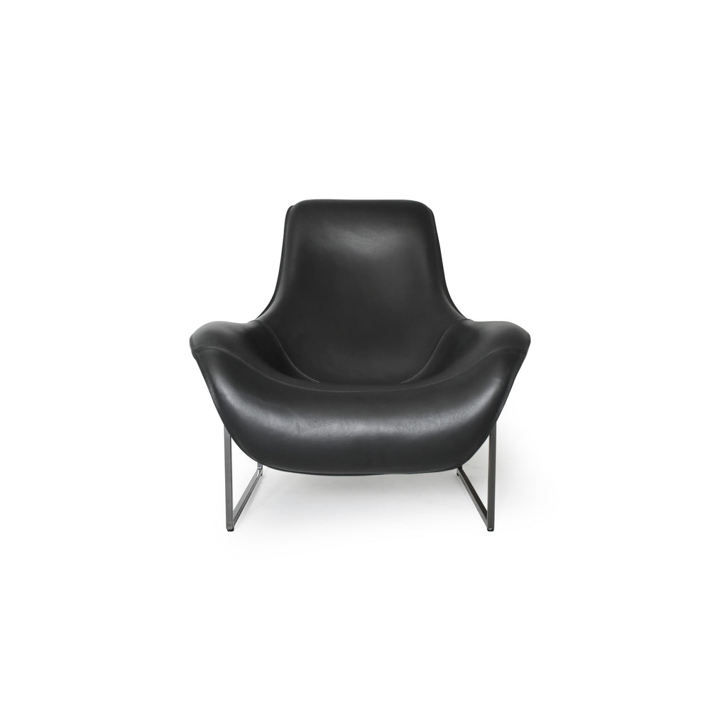 Black leather-like upholstered armchair with curved backrest and integrated armrests, supported by slender metal legs; minimalist form designed for seated comfort in living or reading spaces. Category: furniture/chairs/armchairs