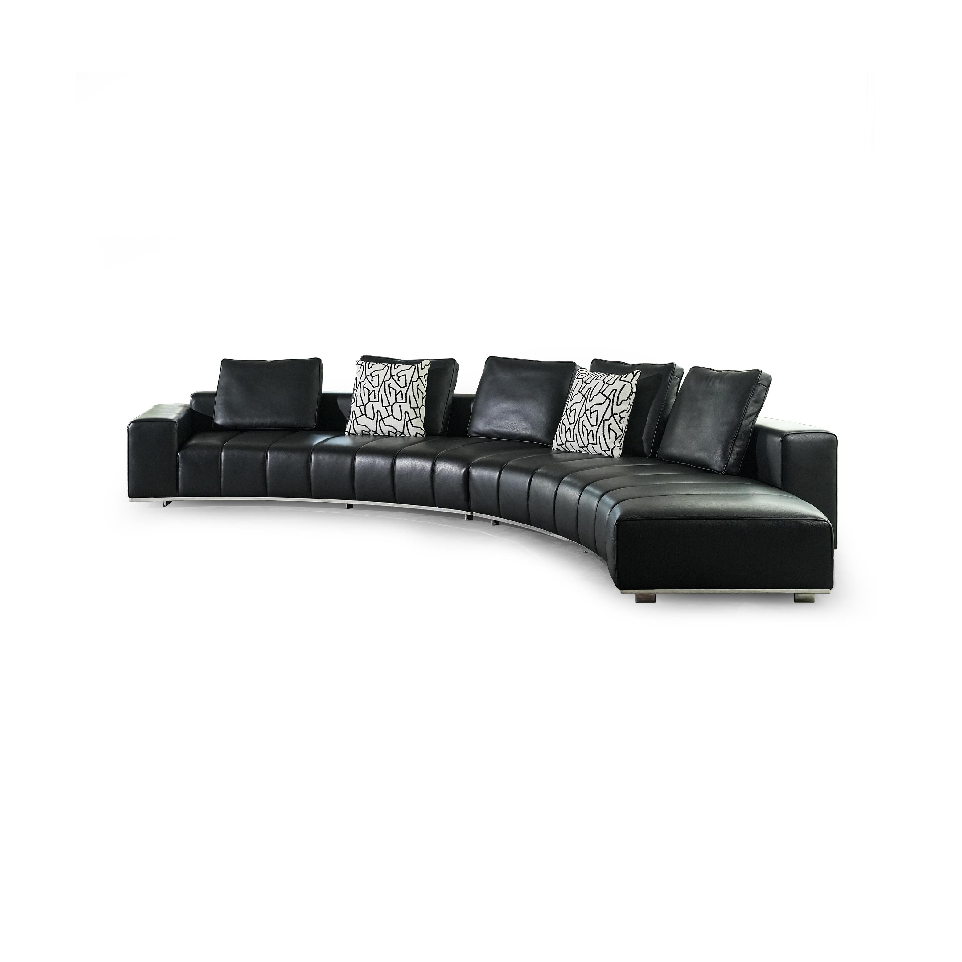 Black leather-like sectional sofa with curved form, featuring segmented cushioning, two patterned throw pillows, and low-profile metal legs; designed for seating and lounging, with visible stitching and defined armrests. Category: furniture/seating/sofas