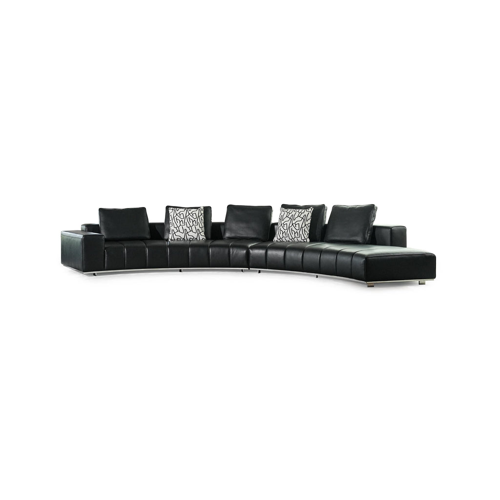 Black leather-like sectional sofa with curved form, featuring segmented cushioning, two patterned throw pillows, and low-profile metal legs; designed for seating and lounging, with visible stitching and defined armrests. Category: furniture/seating/sofas