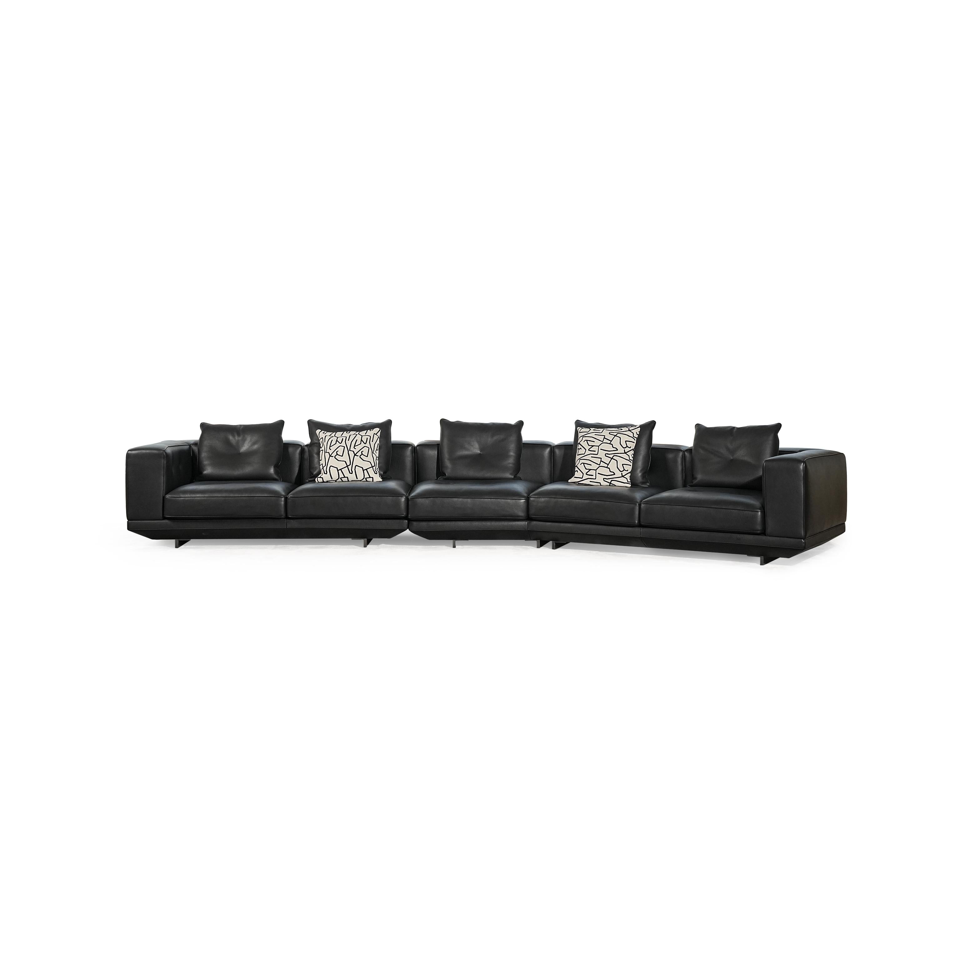 Black leather-like sectional sofa with L-shaped configuration, featuring padded backrests, armrests, and multiple cushions including one with black-and-white geometric pattern and another with zebra print. Low-profile legs support the structure. Intended for seating and lounging. Category: furniture/sofas