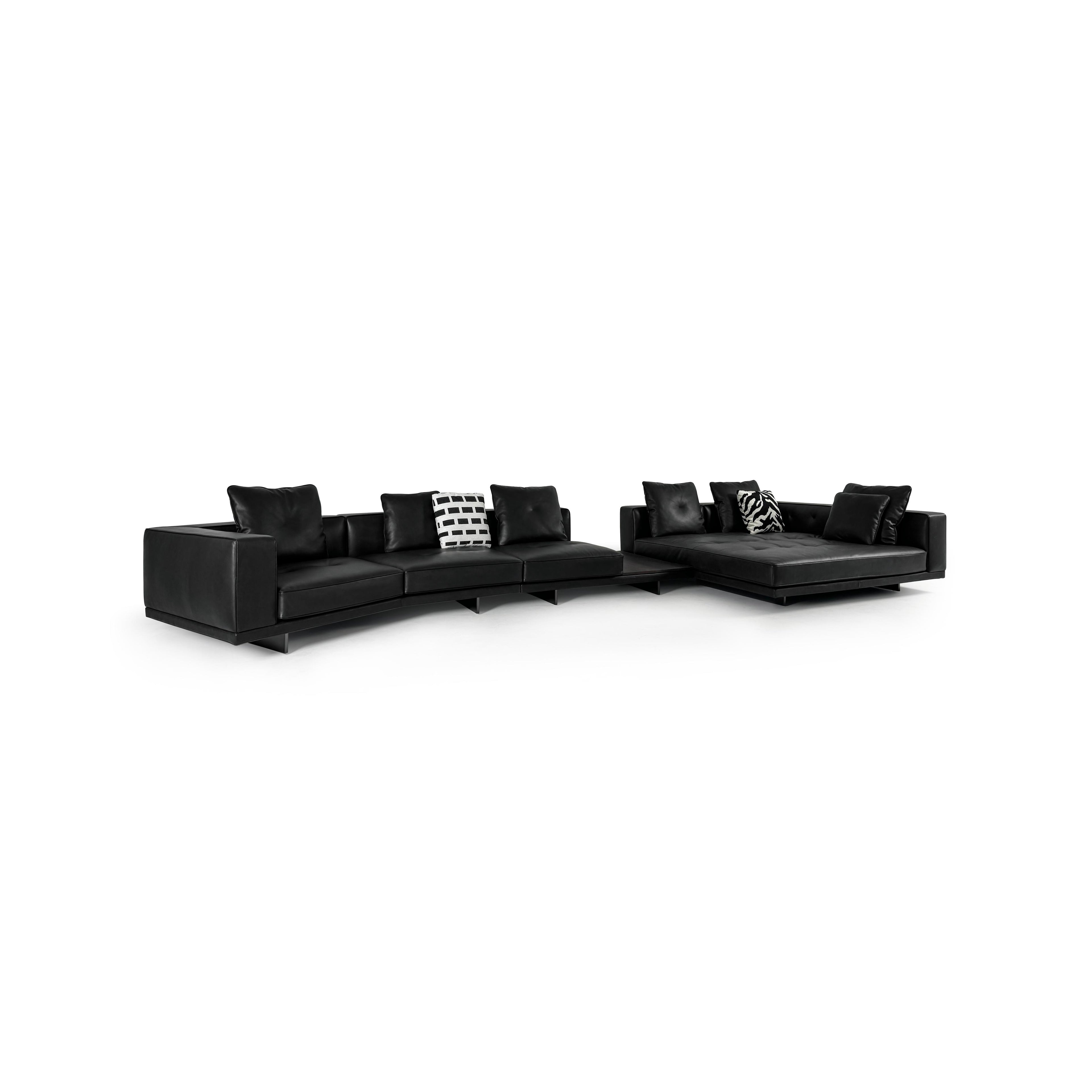Black leather-like sectional sofa with L-shaped configuration, featuring padded backrests, armrests, and multiple cushions including one with black-and-white geometric pattern and another with zebra print. Low-profile legs support the structure. Intended for seating and lounging. Category: furniture/sofas