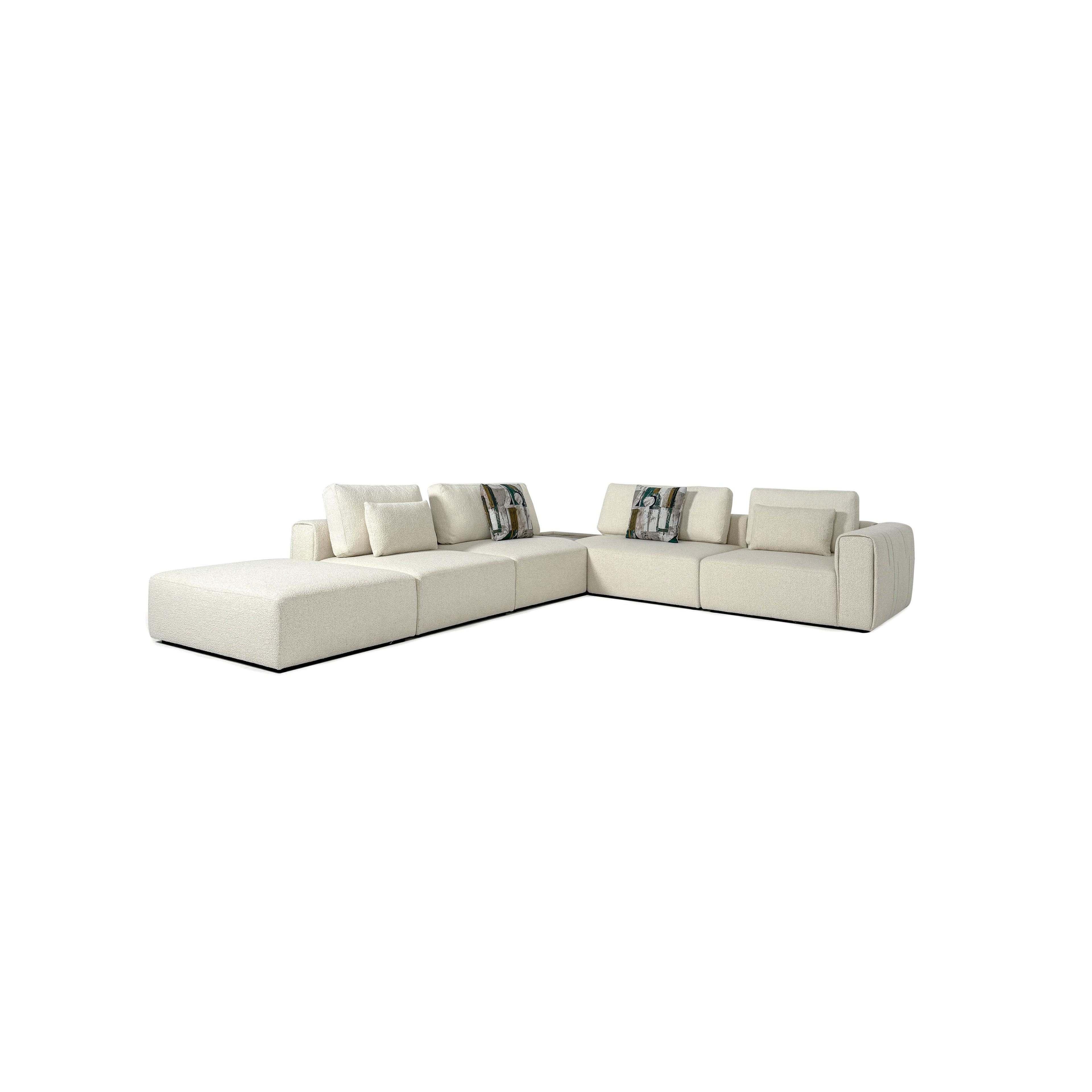 A light beige upholstered sectional sofa with a modular L-shape, featuring thick cushions, soft fabric texture, and two patterned throw pillows, designed for seating and lounging in open spaces. Category: Furniture > Sofas > Sectionals