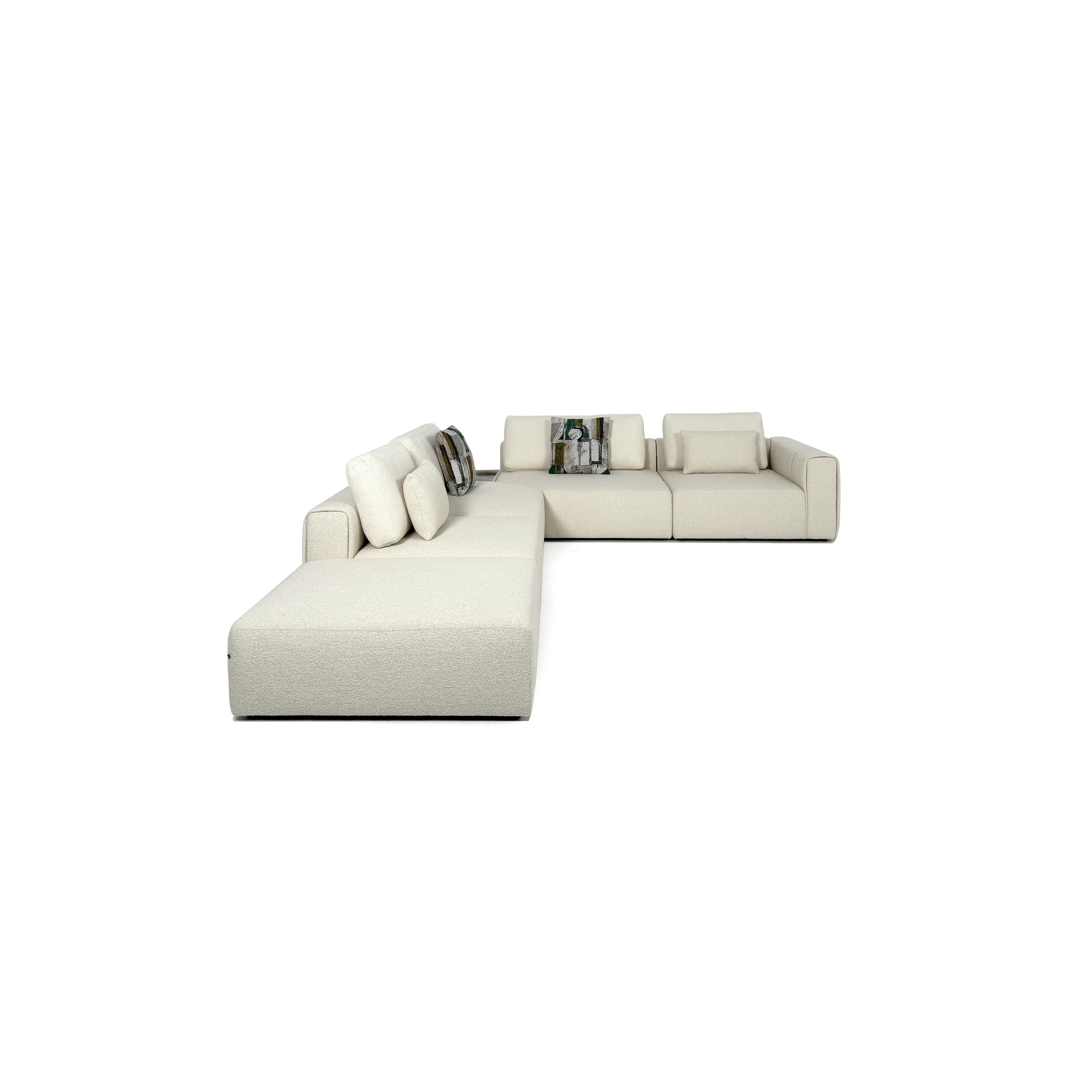 A light beige upholstered sectional sofa with a modular L-shape, featuring thick cushions, soft fabric texture, and two patterned throw pillows, designed for seating and lounging in open spaces. Category: Furniture > Sofas > Sectionals