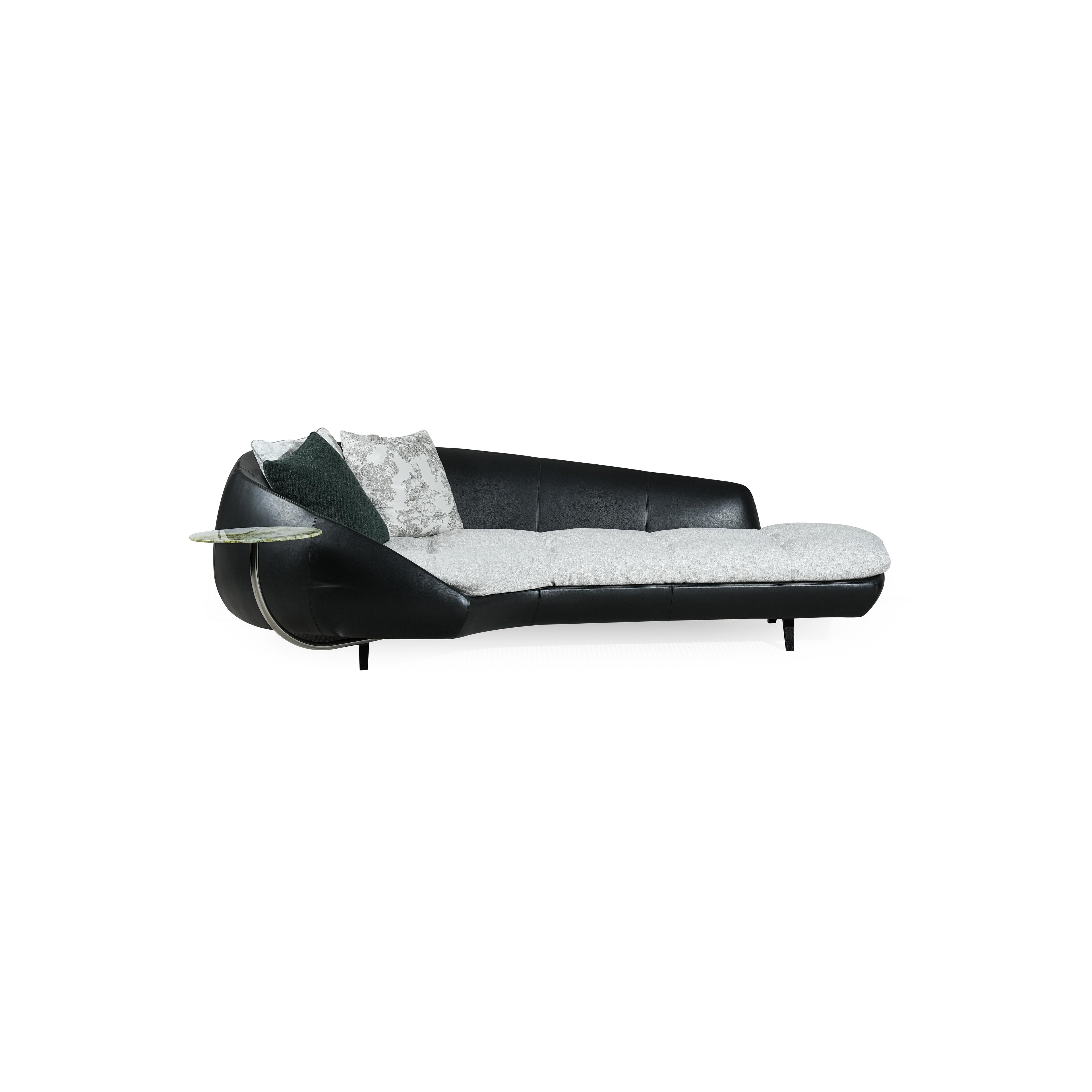 Modern chaise lounge with black leather-like frame and light gray cushioned seat. Curved backrest, single armrest with circular glass table, and four short legs. Two pillows: one dark green, one patterned. Designed for lounging or reclining. Category: Furniture > Sofas & Chaises