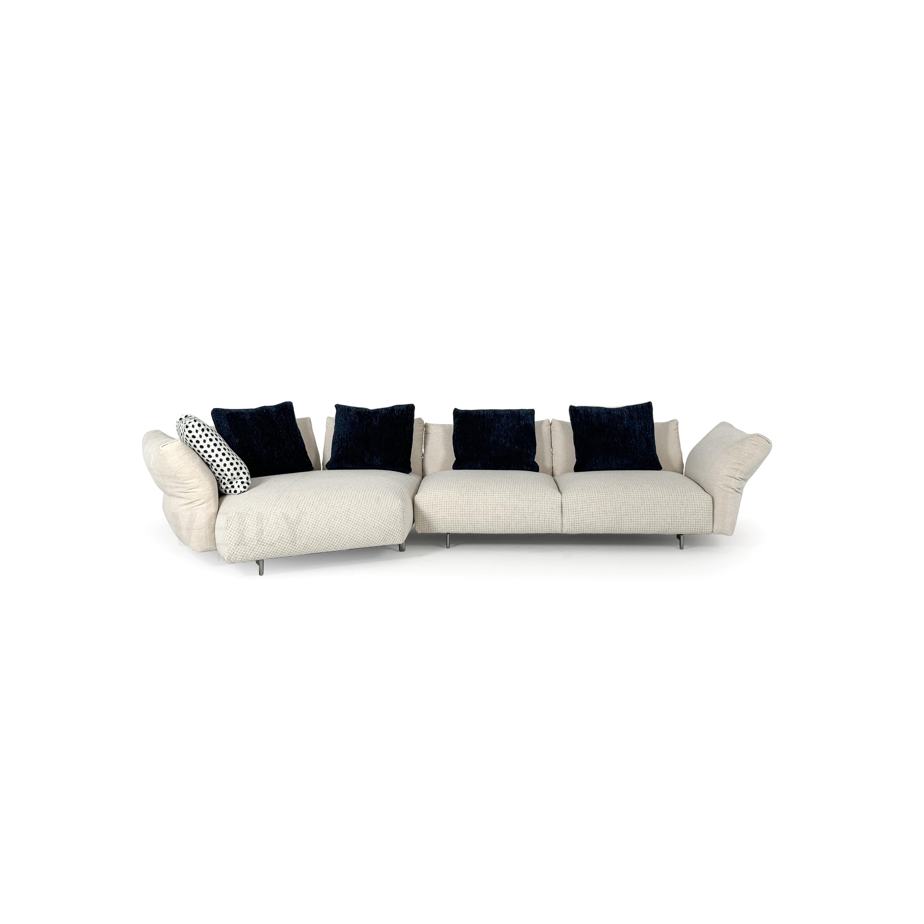 A three-seater sectional sofa with light beige fabric upholstery and dark navy velvet cushions. It features curved armrests, segmented seat cushions, and thin metal legs. The left end includes a chaise lounge with a polka-dot accent pillow. Designed for seating and lounging. Category: furniture/sofas