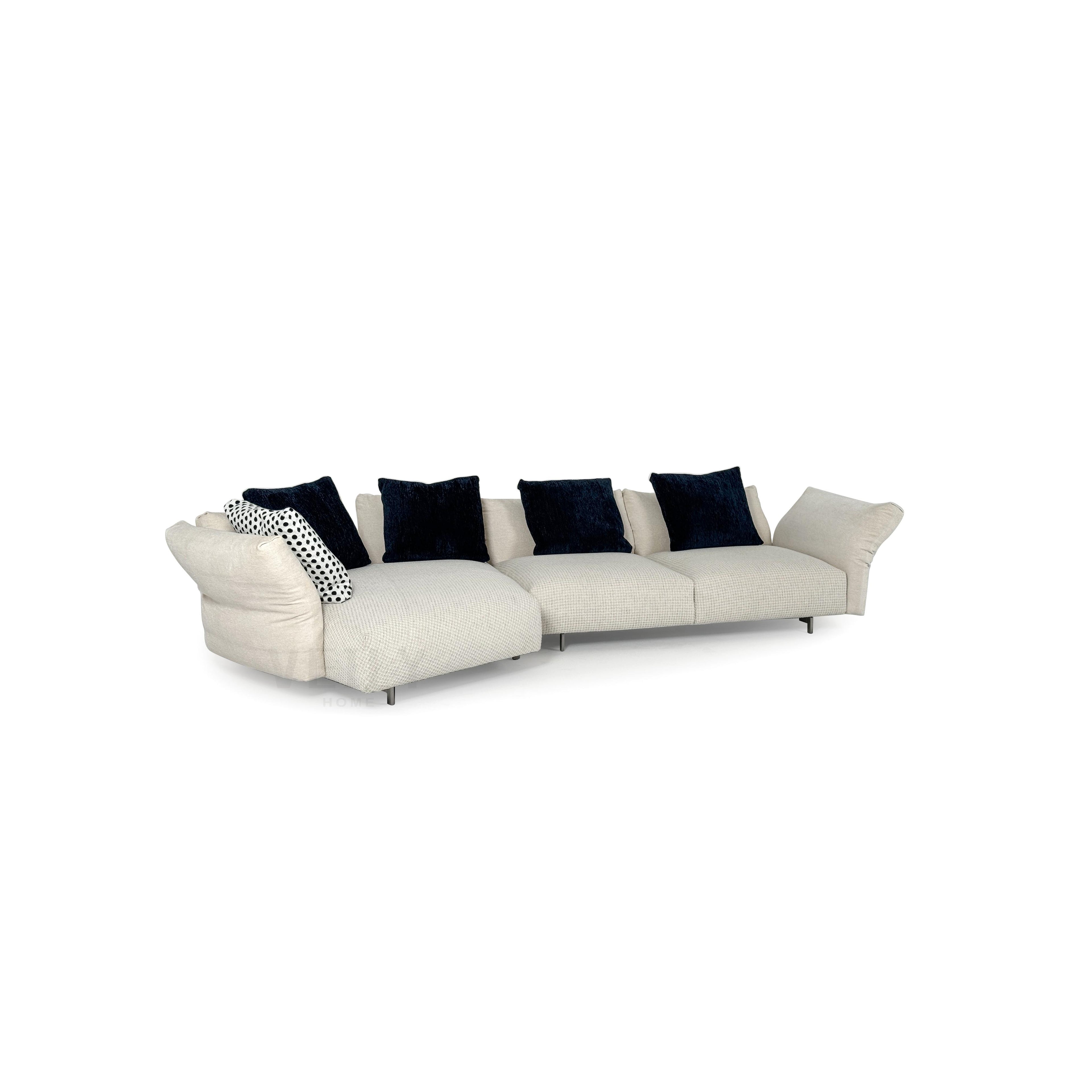 A three-seater sectional sofa with light beige fabric upholstery and dark navy velvet cushions. It features curved armrests, segmented seat cushions, and thin metal legs. The left end includes a chaise lounge with a polka-dot accent pillow. Designed for seating and lounging. Category: furniture/sofas