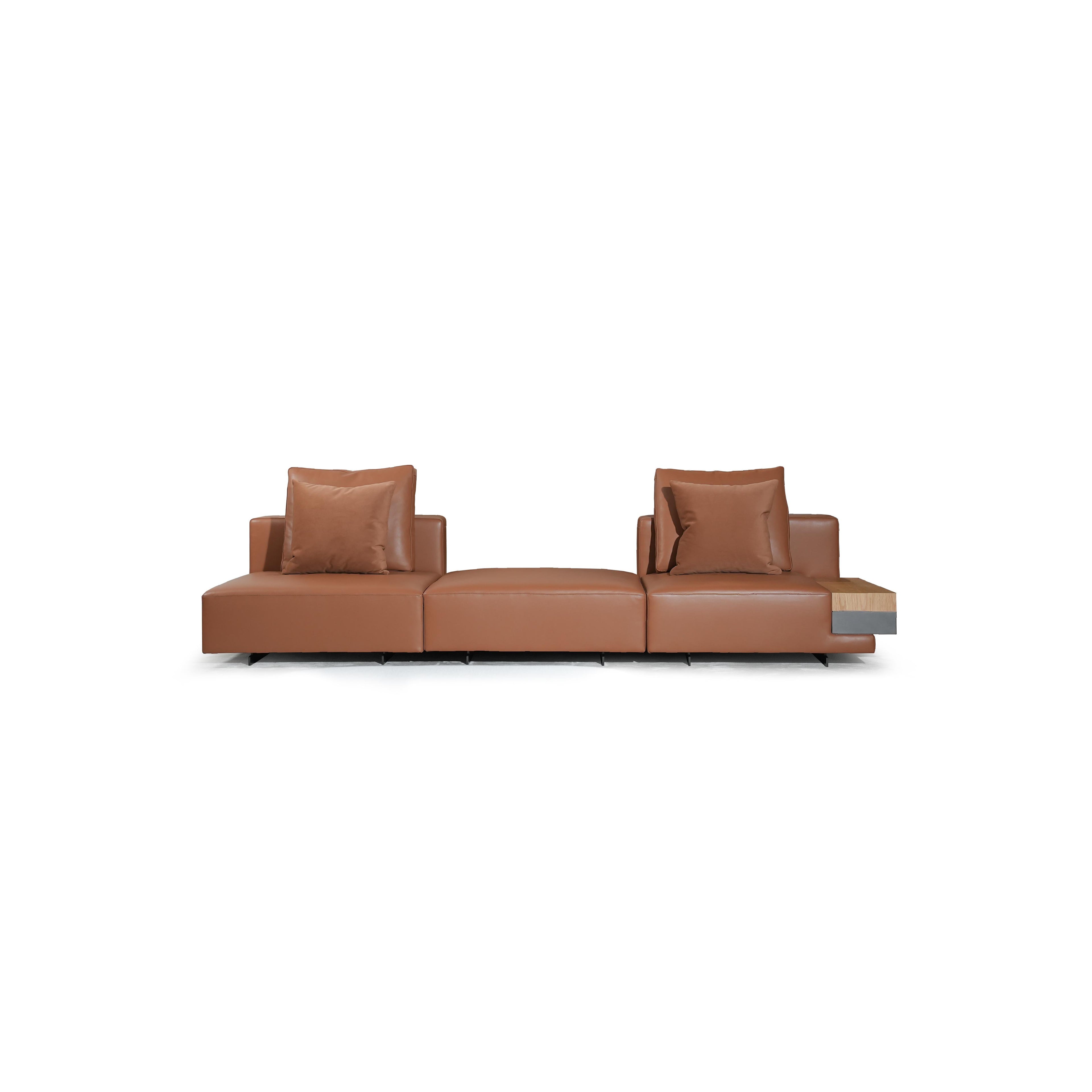 Brown leather-like sofa with three rectangular seat sections, two armrests, and two back cushions. Each section has a matching cushion. Right end features a wooden and dark gray panel. Supported by black legs. Intended for seating. Category: furniture/sofas