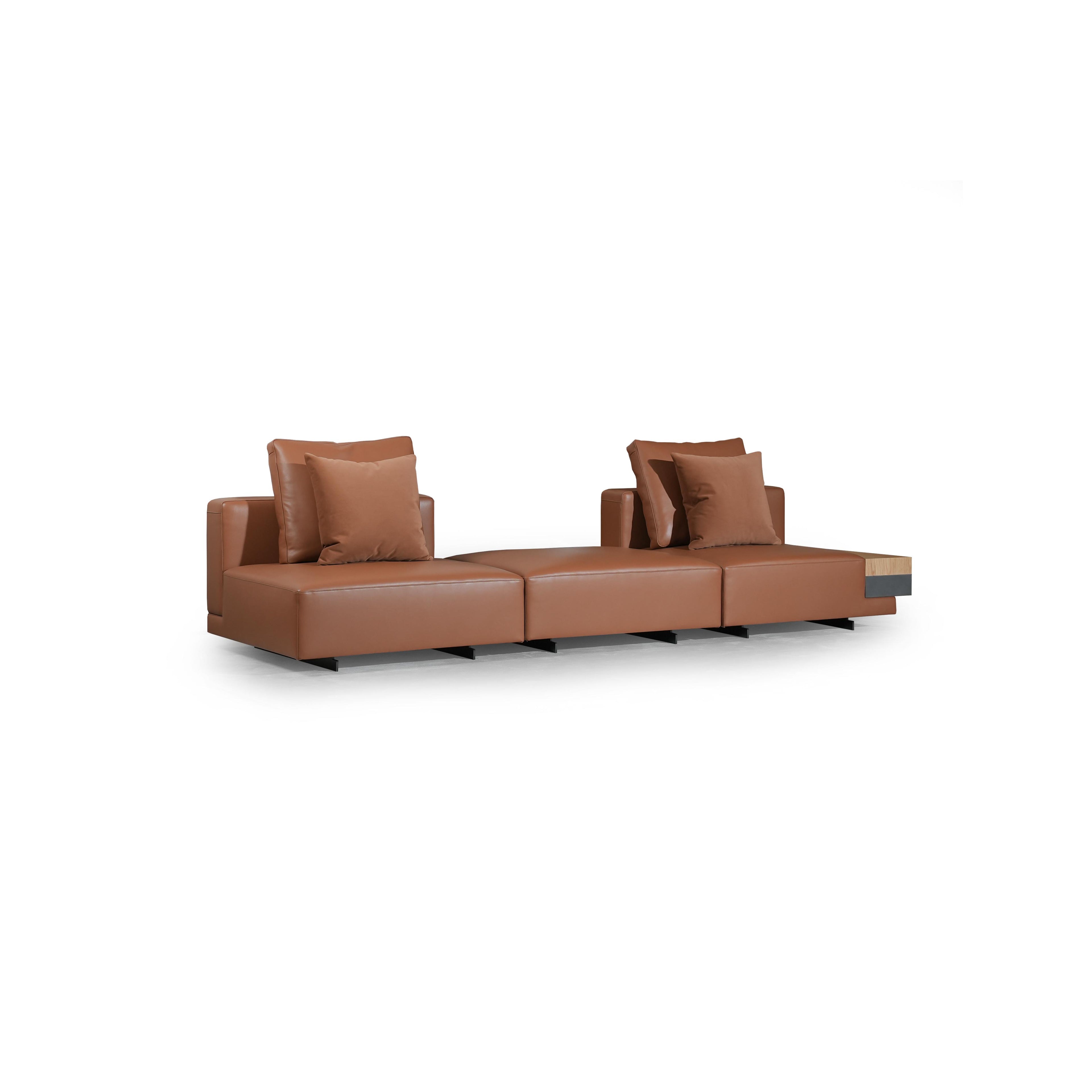 Brown leather-like sofa with three rectangular seat sections, two armrests, and two back cushions. Each section has a matching cushion. Right end features a wooden and dark gray panel. Supported by black legs. Intended for seating. Category: furniture/sofas