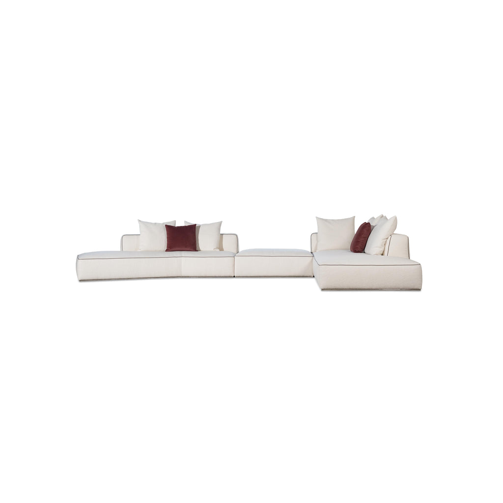 This is a modular sectional sofa with a low-profile, L-shaped form. It features white fabric upholstery with contrasting dark red accent pillows. The sofa has defined armrests, segmented cushioning, and visible stitching along edges. Designed for seating, it includes multiple cushioned sections for comfort. Category: furniture/sofas