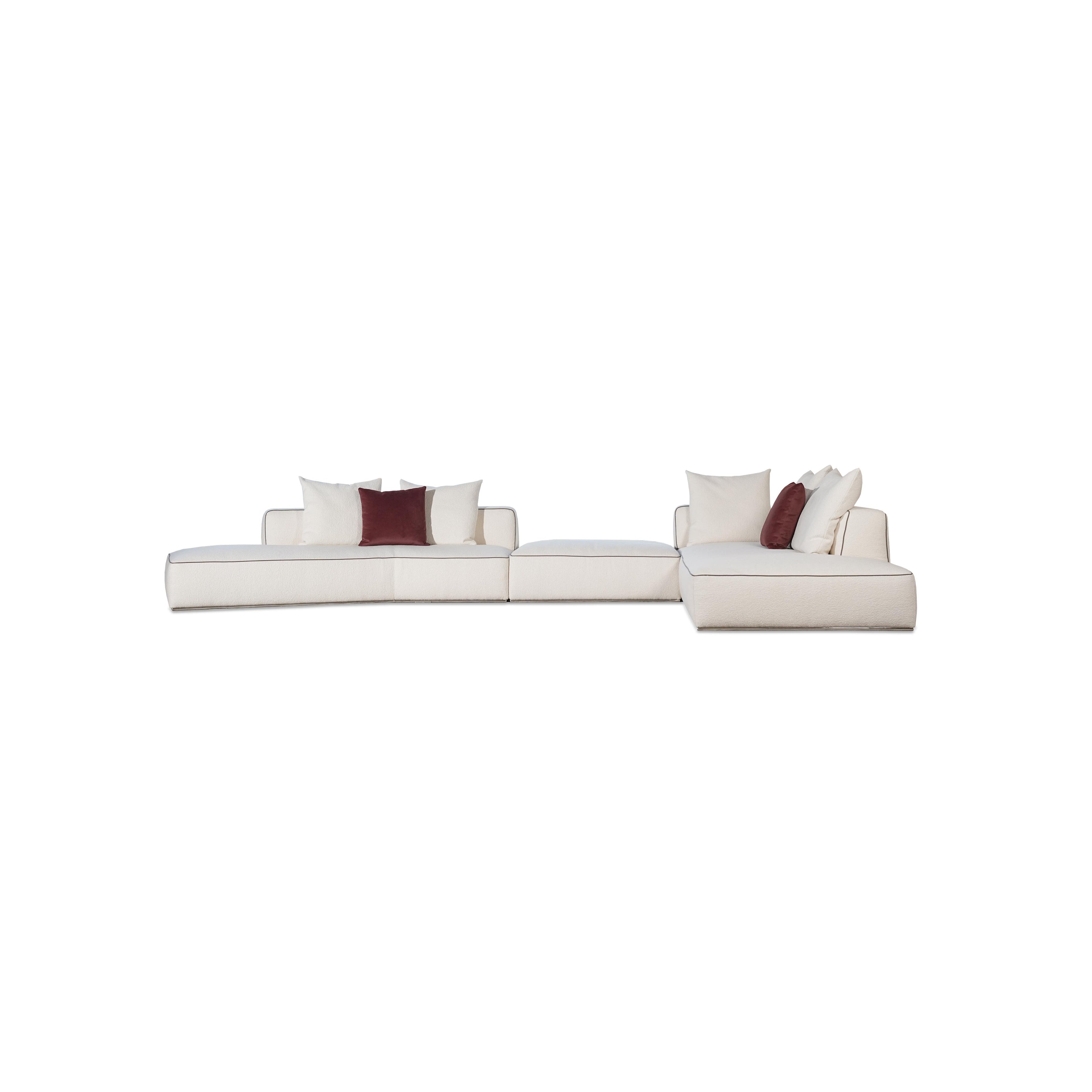 This is a modular sectional sofa with a low-profile, L-shaped form. It features white fabric upholstery with contrasting dark red accent pillows. The sofa has defined armrests, segmented cushioning, and visible stitching along edges. Designed for seating, it includes multiple cushioned sections for comfort. Category: furniture/sofas
