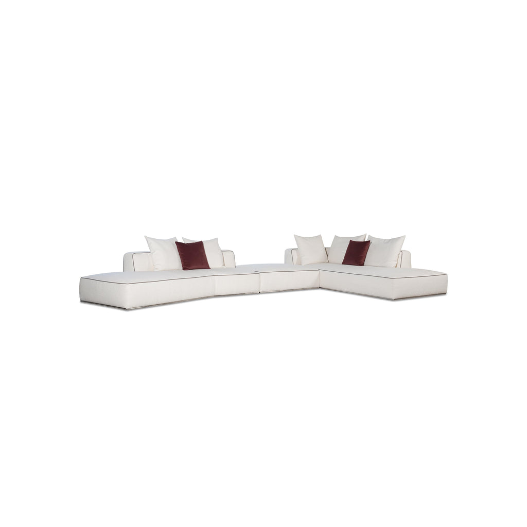 This is a modular sectional sofa with a low-profile, L-shaped form. It features white fabric upholstery with contrasting dark red accent pillows. The sofa has defined armrests, segmented cushioning, and visible stitching along edges. Designed for seating, it includes multiple cushioned sections for comfort. Category: furniture/sofas
