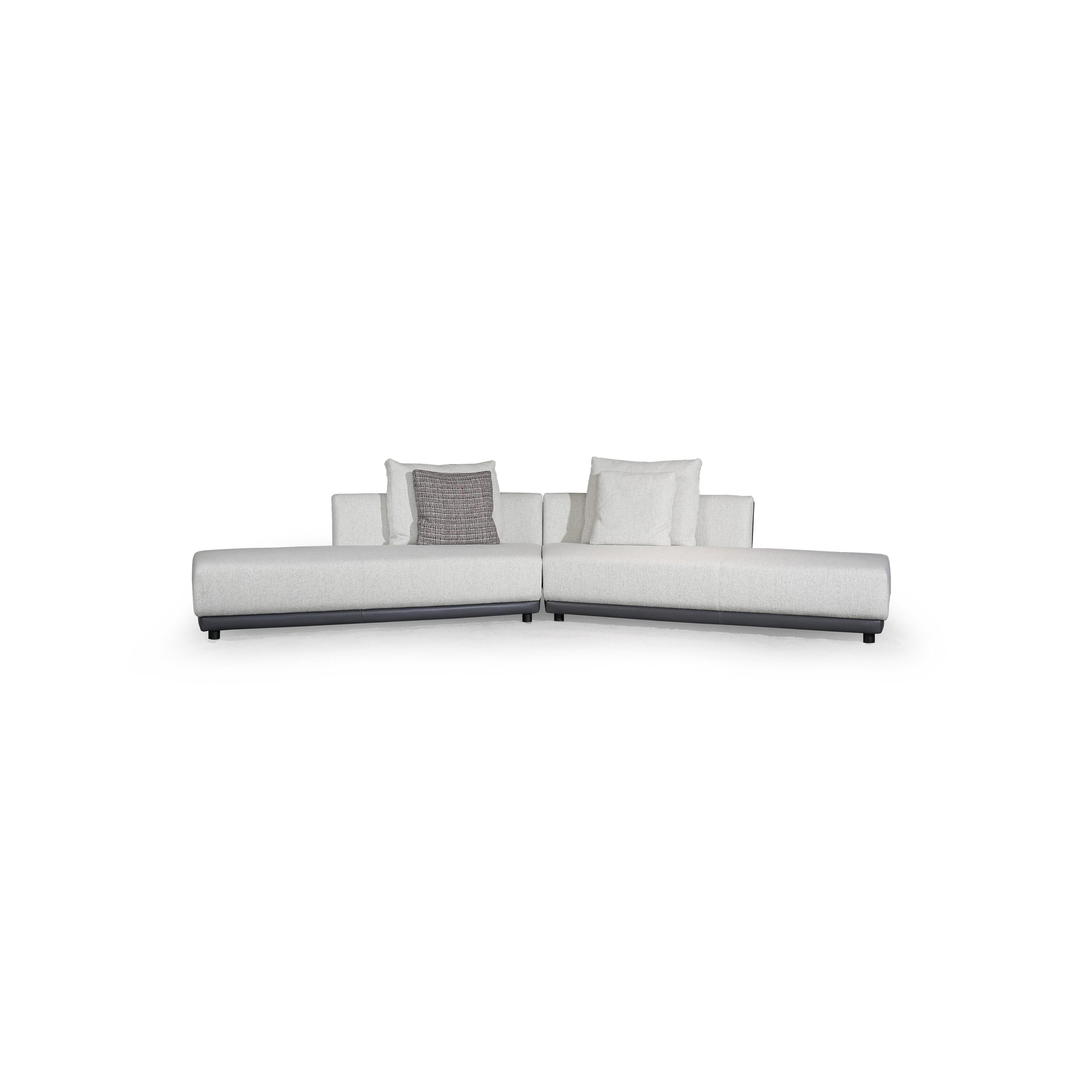 L-shaped sectional sofa with off-white fabric upholstery and dark gray armrests and base. Features multiple cushions, including two textured throw pillows. Supported by short, dark legs. Designed for seating and lounging. Category: furniture/sofas