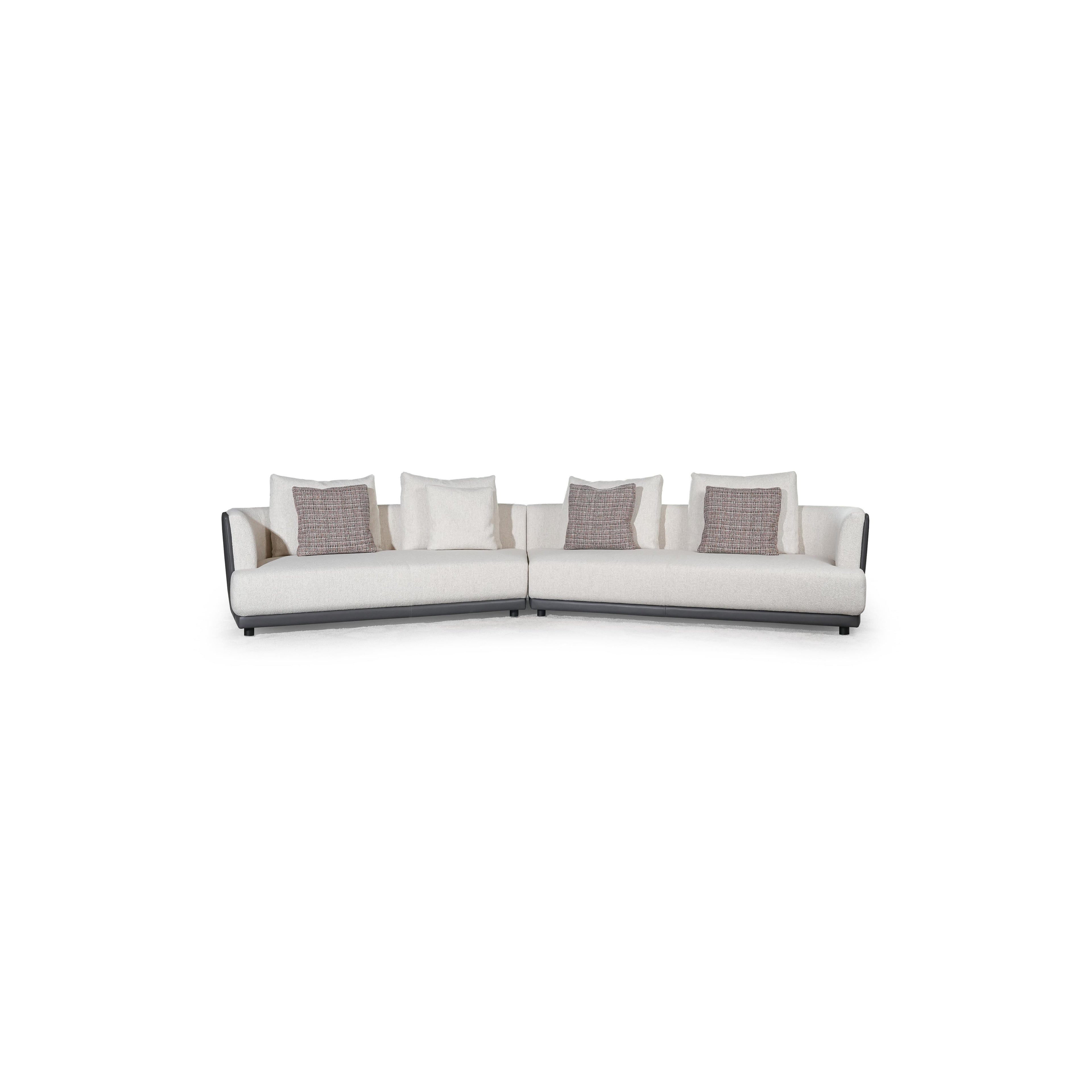 L-shaped sectional sofa with off-white fabric upholstery and dark gray armrests and base. Features multiple cushions, including two textured throw pillows. Supported by short, dark legs. Designed for seating and lounging. Category: furniture/sofas