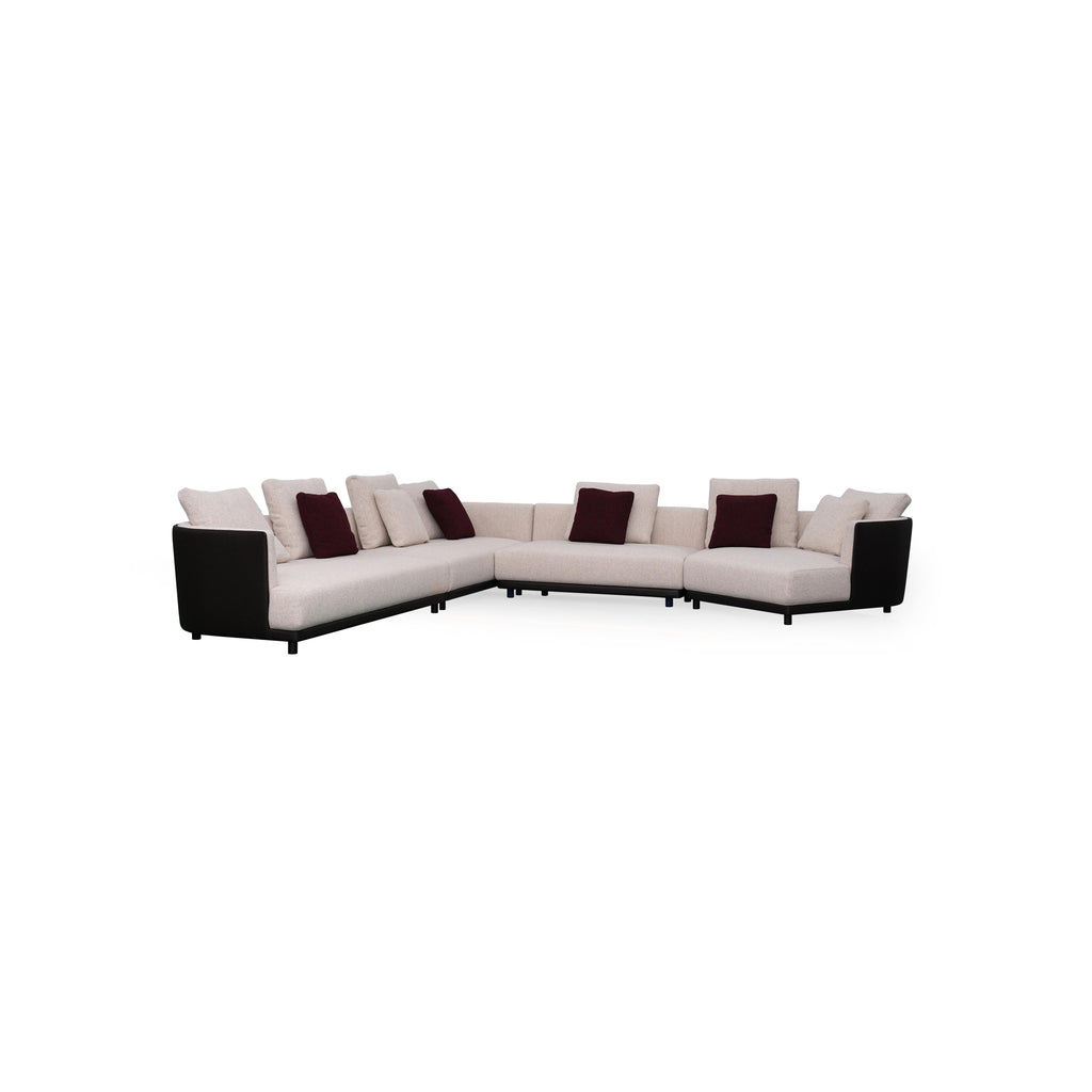 L-shaped sectional sofa with off-white fabric upholstery and dark gray armrests and base. Features multiple cushions, including two textured throw pillows. Supported by short, dark legs. Designed for seating and lounging. Category: furniture/sofas