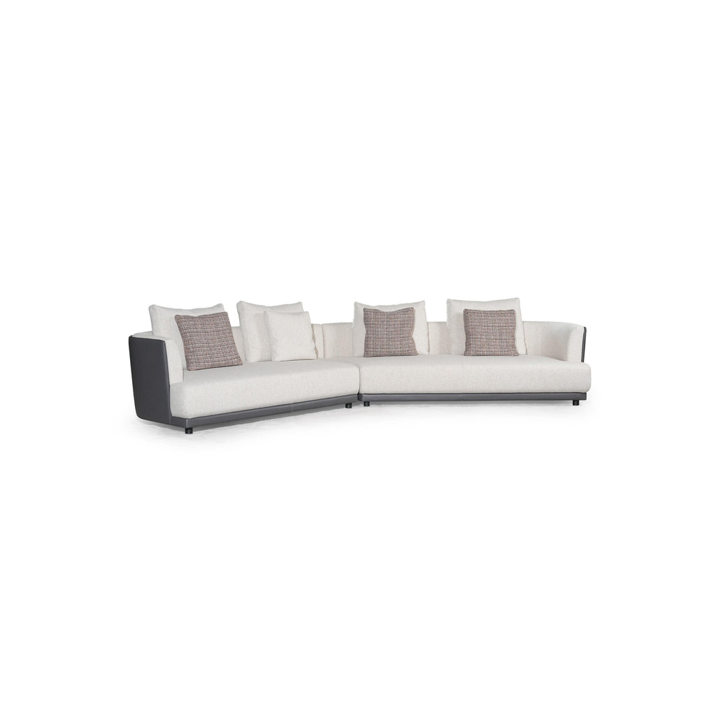 L-shaped sectional sofa with off-white fabric upholstery and dark gray armrests and base. Features multiple cushions, including two textured throw pillows. Supported by short, dark legs. Designed for seating and lounging. Category: furniture/sofas