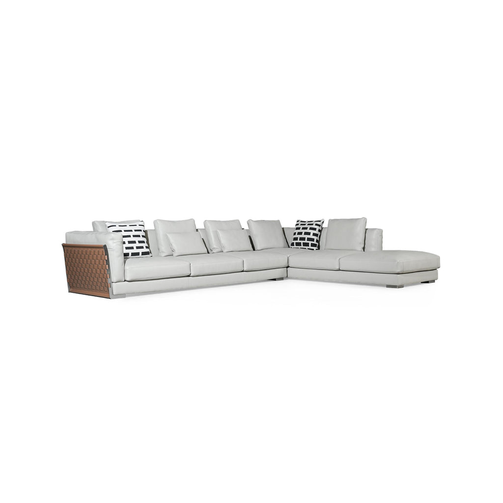 This is a sectional sofa with light gray upholstery and a brown woven panel on the left armrest. It has multiple cushions, including two black-and-white patterned pillows. The sofa has low-profile legs and a continuous backrest. It is designed for seating and lounging. Category: furniture/sofas